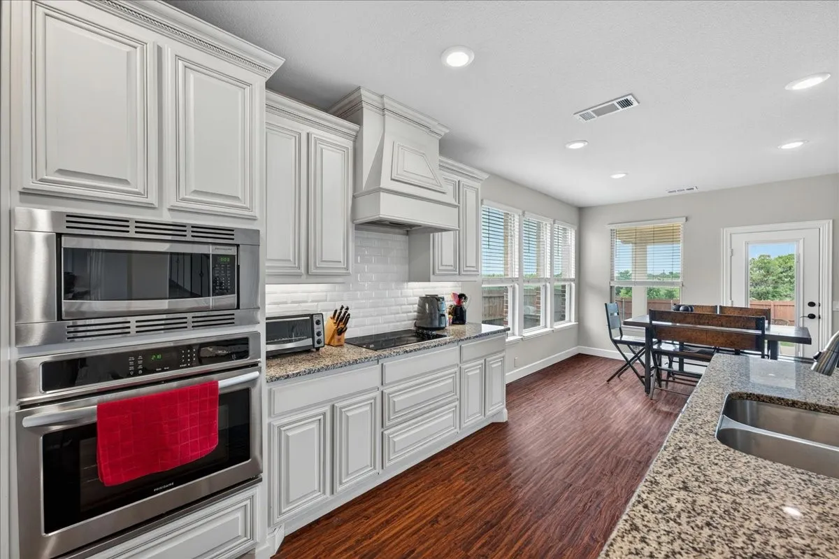 Sophisticated kitchen featuring white cabinetry with detailed molding, stainless steel appliances including a double wall oven and microwave, granite countertops, subway tile backsplash, and pendant lighting