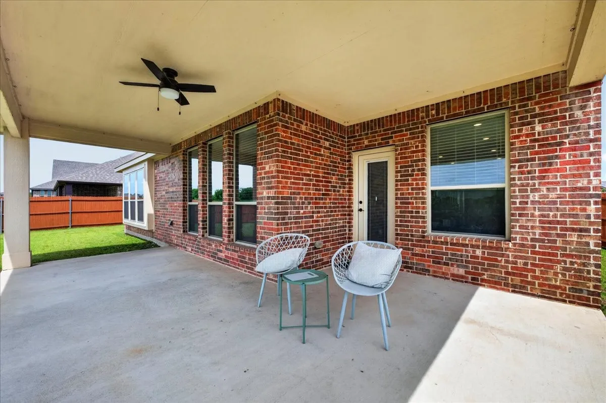 Covered patio featuring a ceiling fan, brick exterior, multiple windows, and a fenced yard