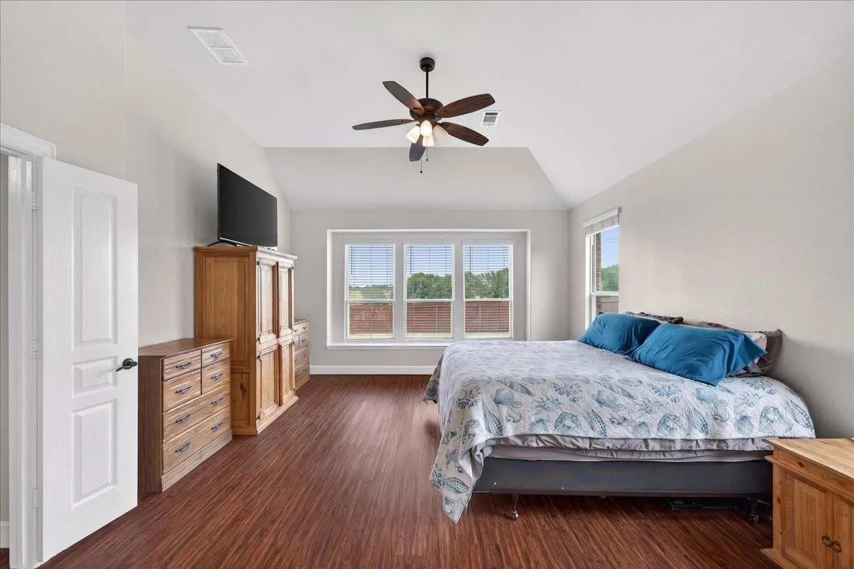 Spacious room featuring wood-finish flooring, vaulted ceilings, and a ceiling fan
