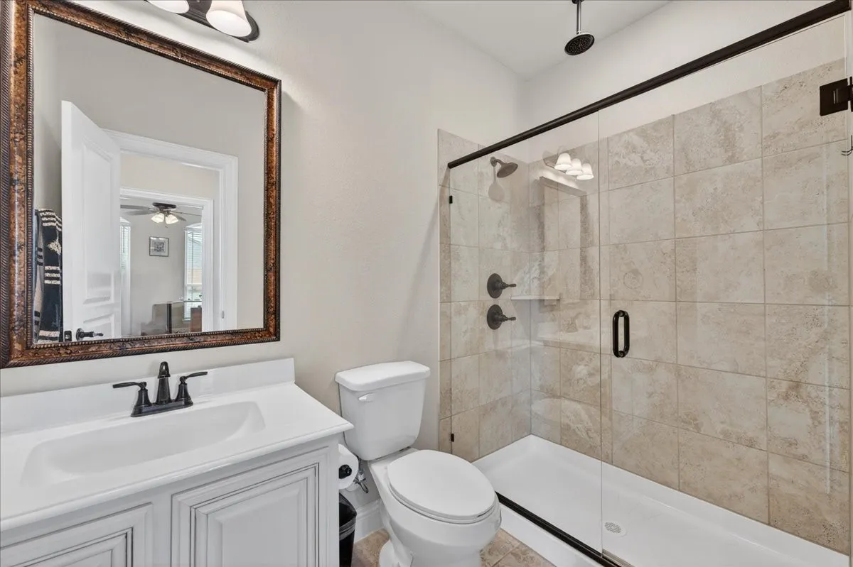 Front Hall Bathroom featuring a glass-enclosed shower with tile surround, white vanity cabinet with countertop sink, a framed mirror and rain shower.