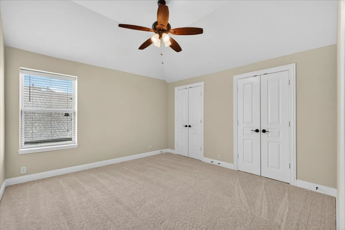 2nd bedroom is spacious room featuring vaulted ceilings, light beige carpeting, and two sets of white bi-fold doors