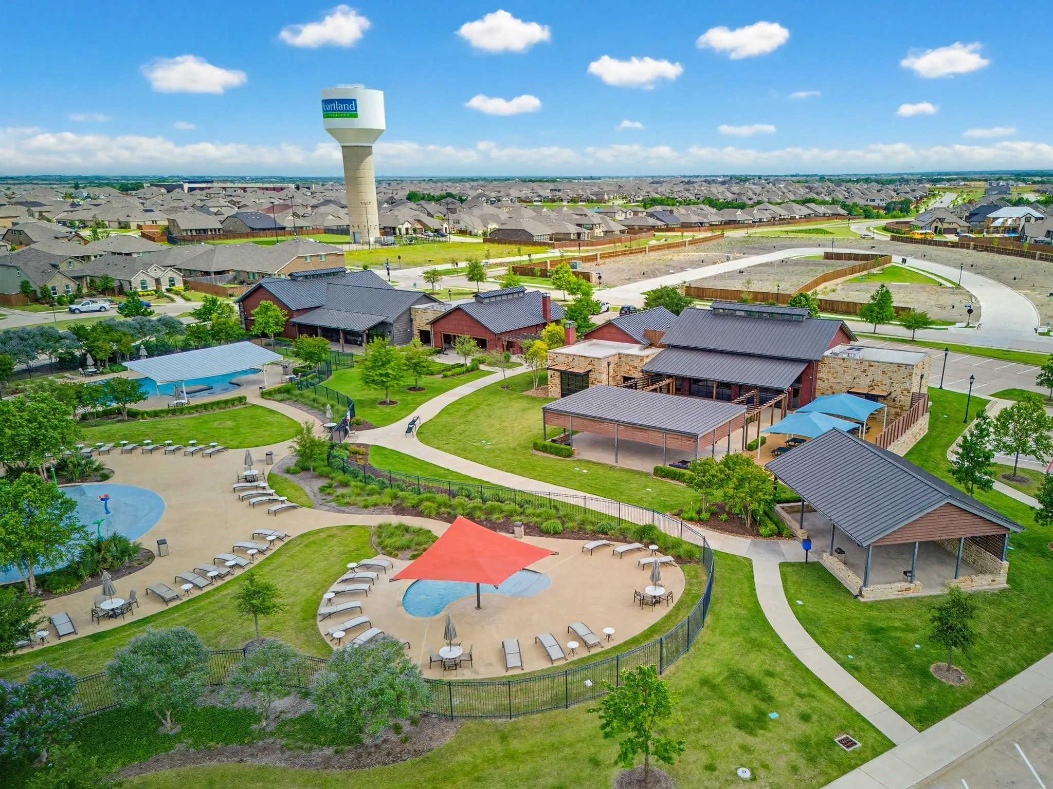 Community amenity center featuring multiple pools, expansive green spaces, shaded gathering areas, and extensive walking paths