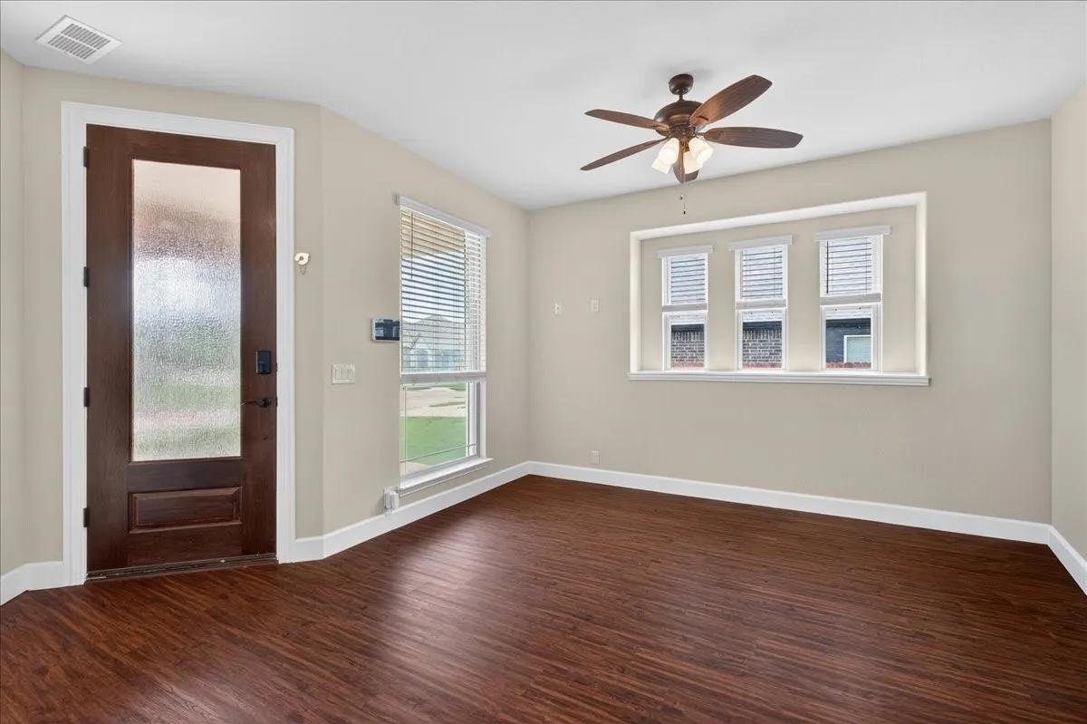 Bright and spacious room featuring rich wood-finish flooring, neutral wall finishes, and abundant natural light from multiple windows with plantation shutters