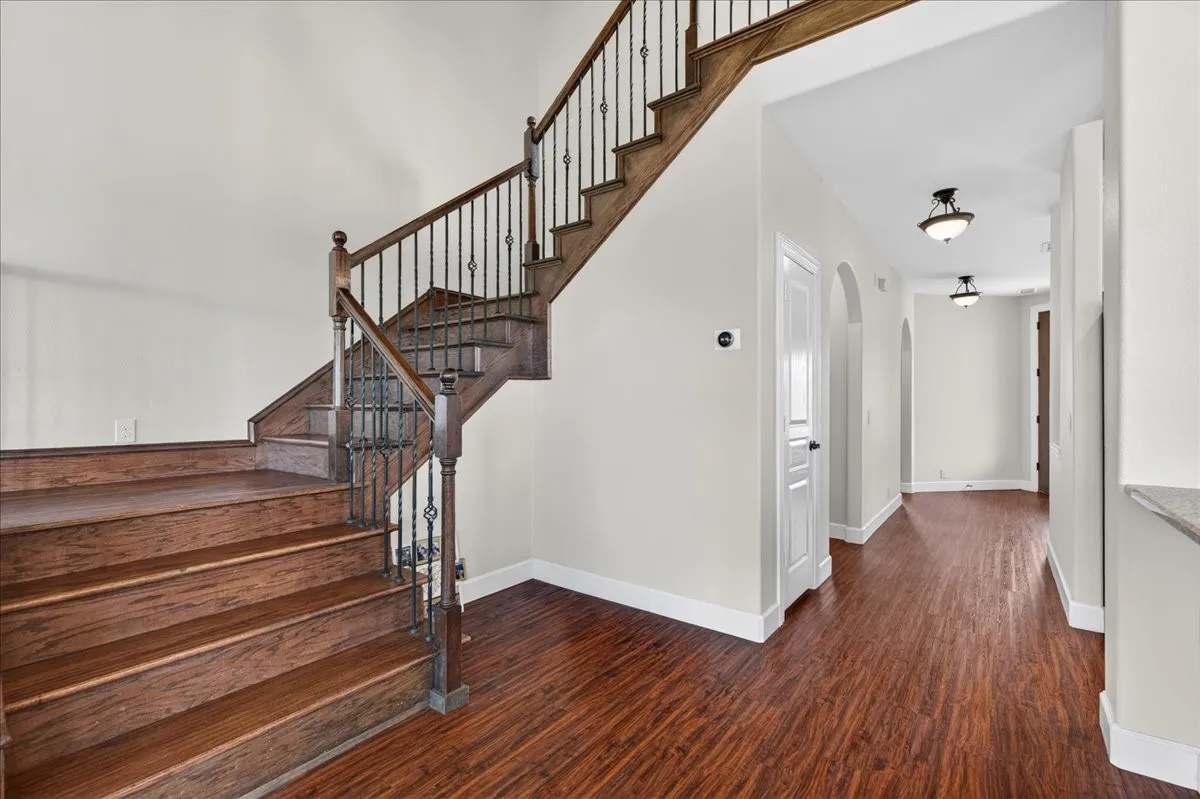 Wood-finish flooring throughout, featuring a staircase with wood treads and wrought iron balusters
