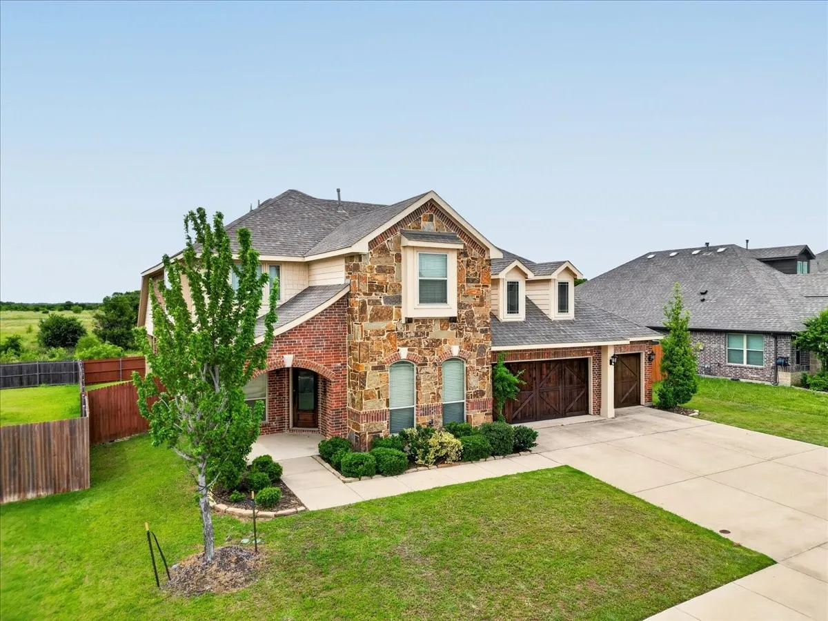 Stone and brick exterior with a prominent front entry, attached two-car garage with wood-finish doors, and a concrete driveway