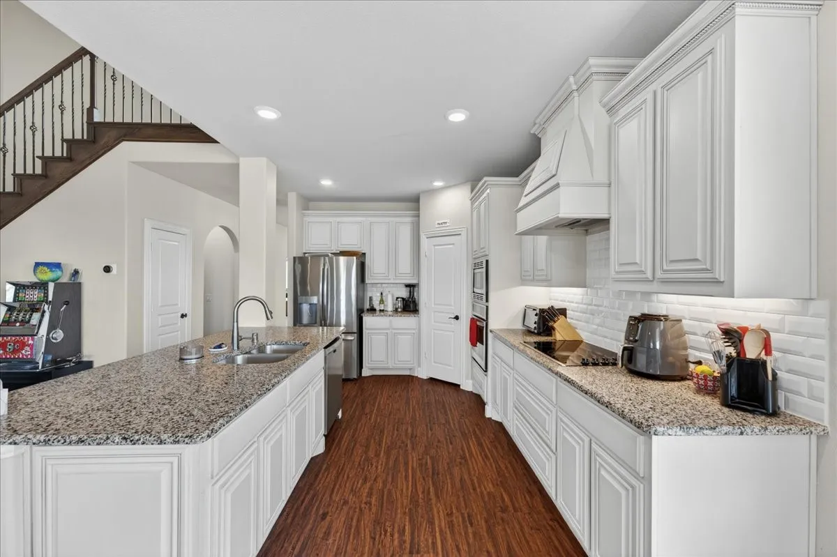 Spacious kitchen featuring an expansive island with an undermount sink, granite countertops, white cabinetry with crown molding, and wood-finish flooring