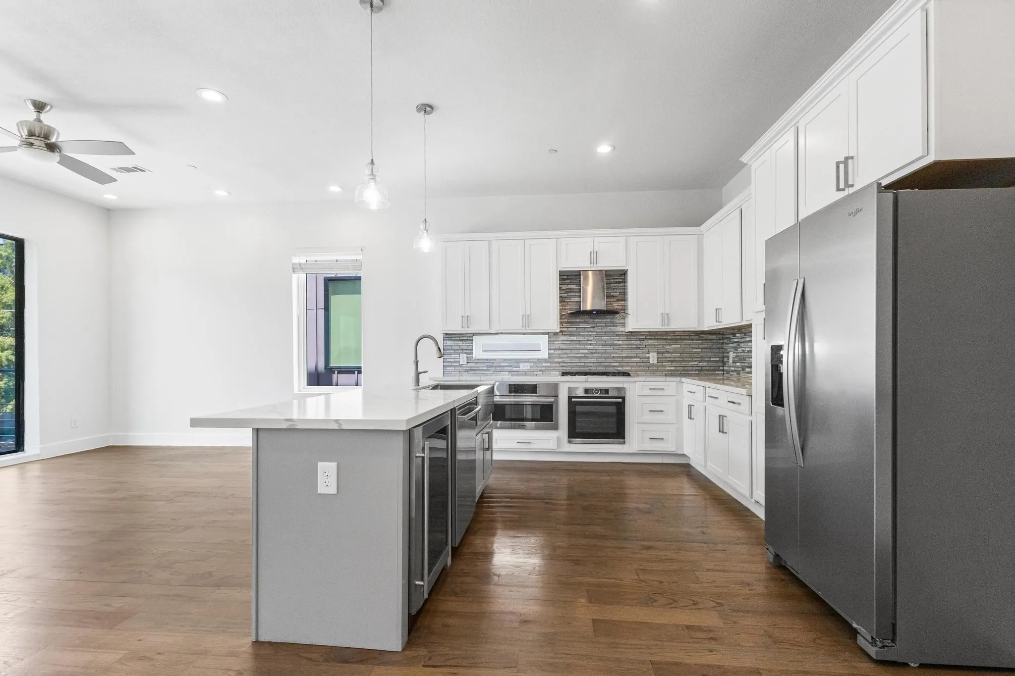 Open-concept kitchen with white shaker cabinetry, stainless steel appliances, a tile backsplash, and an island featuring integrated beverage coolers