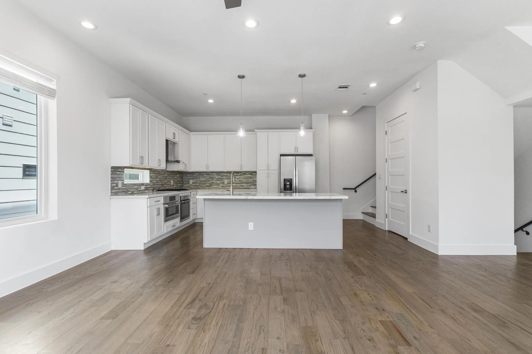 Open-concept kitchen with white cabinetry and a central island, stainless steel appliances, mosaic tile backsplash, wood-finish flooring, and recessed lighting