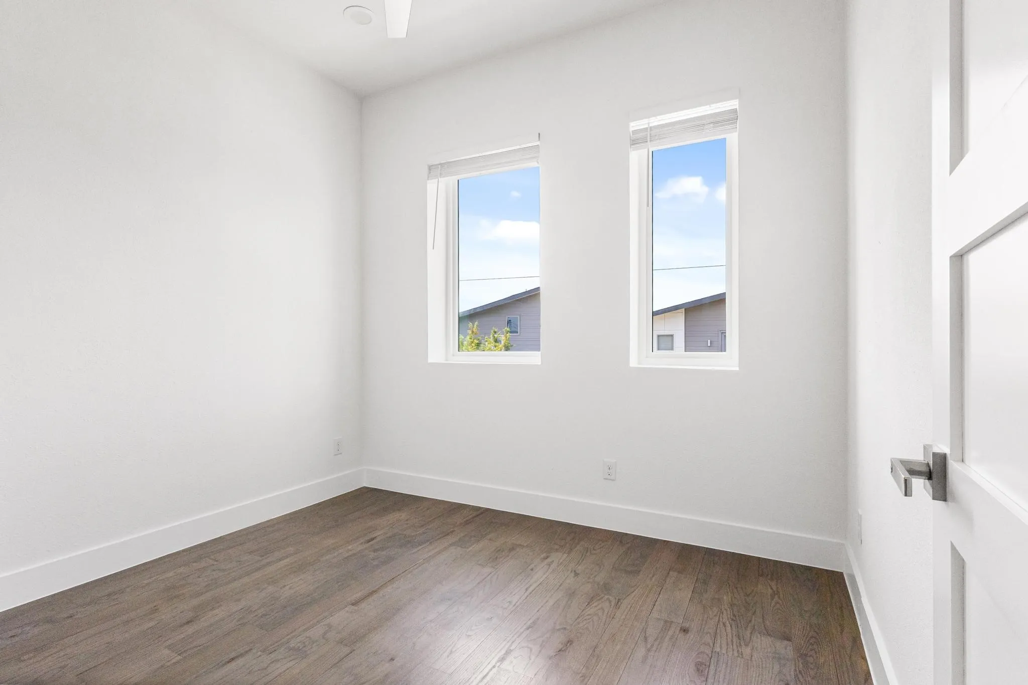 Wood-finish flooring, white walls, and two rectangular windows with blinds