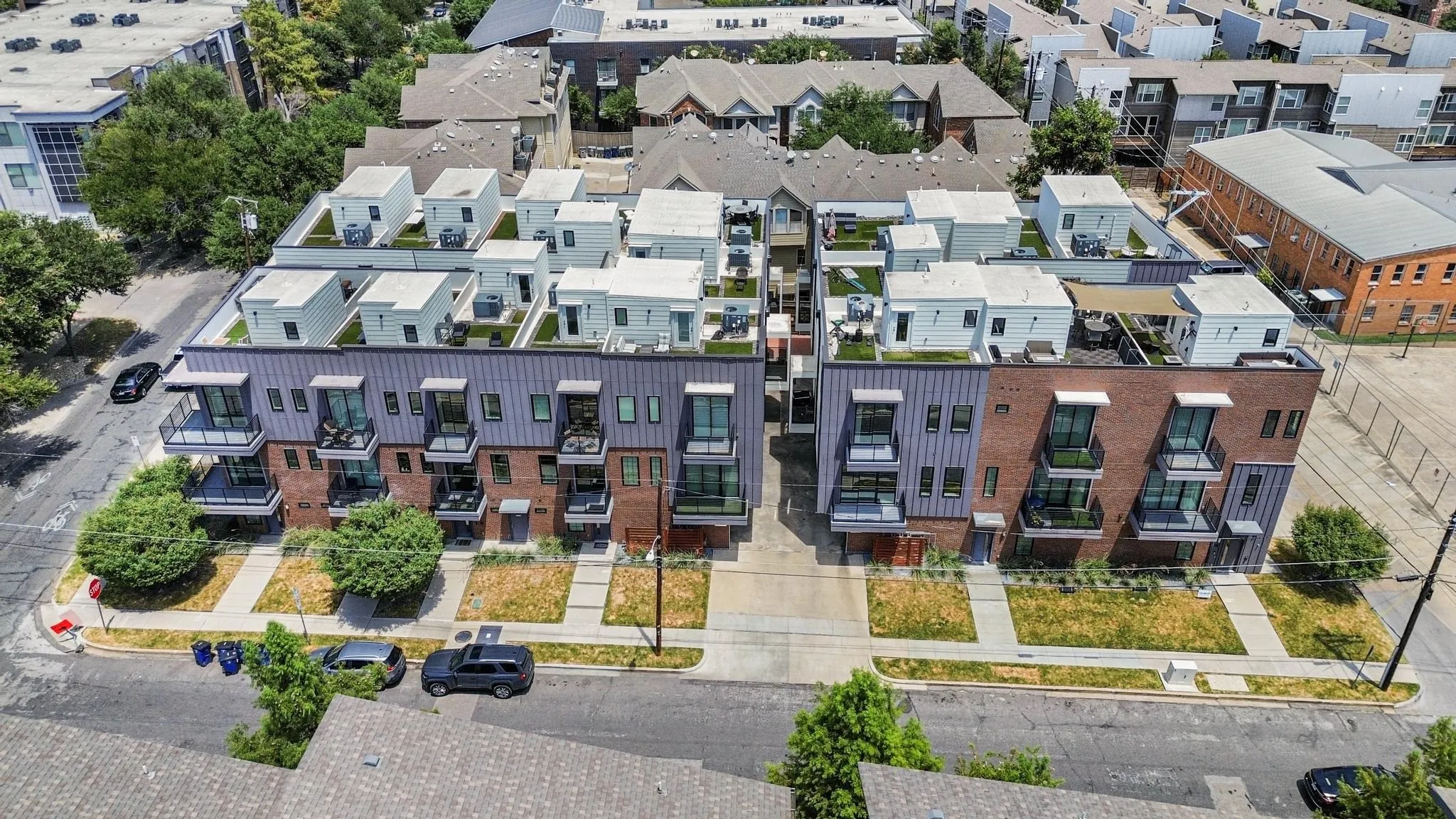 Modern multi-story buildings featuring brick and vertical siding exteriors, private balconies with dark railings, and rooftop terraces