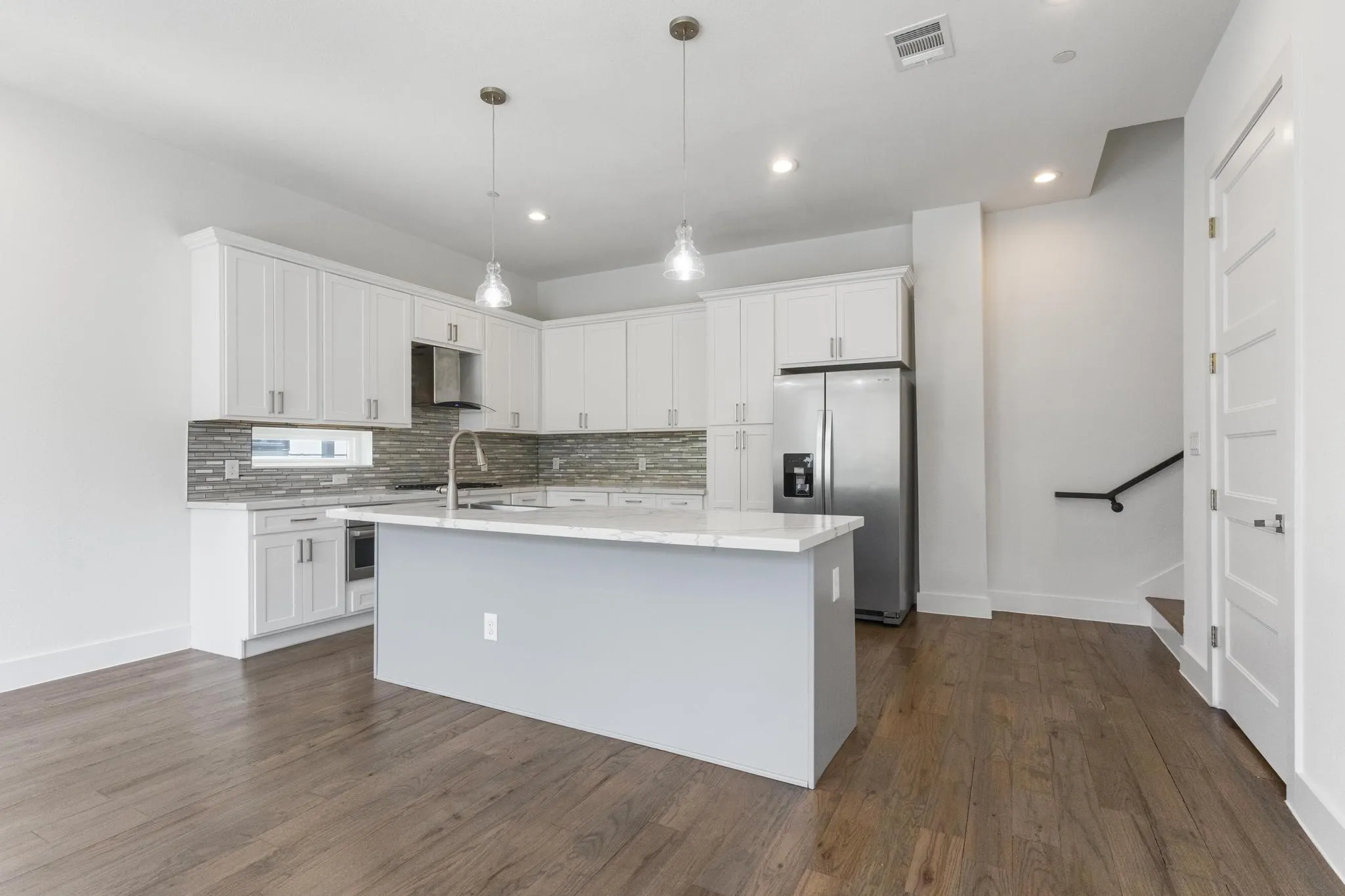 Kitchen featuring white cabinetry, a large center island with a light-toned countertop, stainless steel appliances, a tiled backsplash, and wood-finish flooring