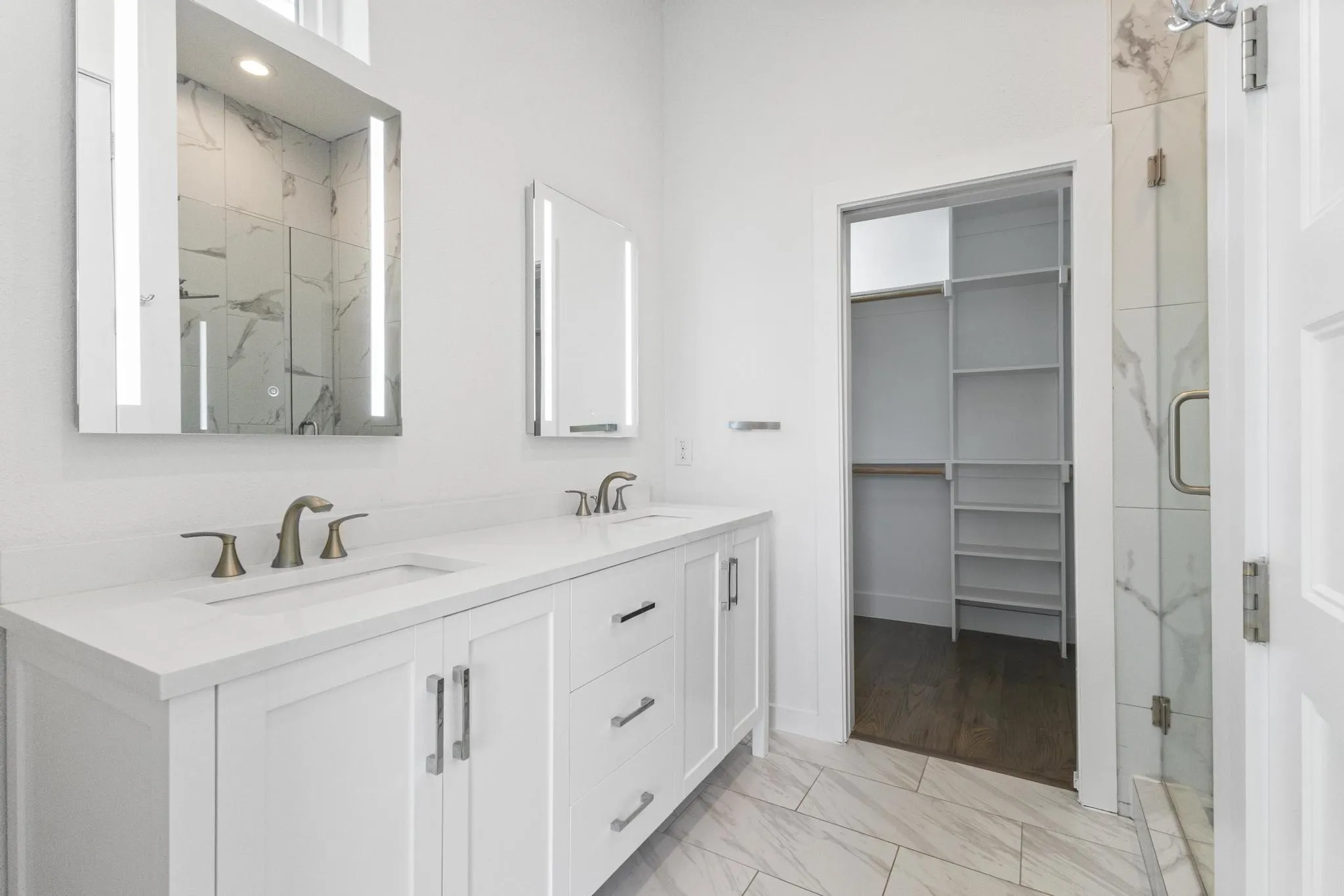 Dual vanity with integrated sinks, illuminated mirrors, a glass-enclosed shower, and a custom closet system