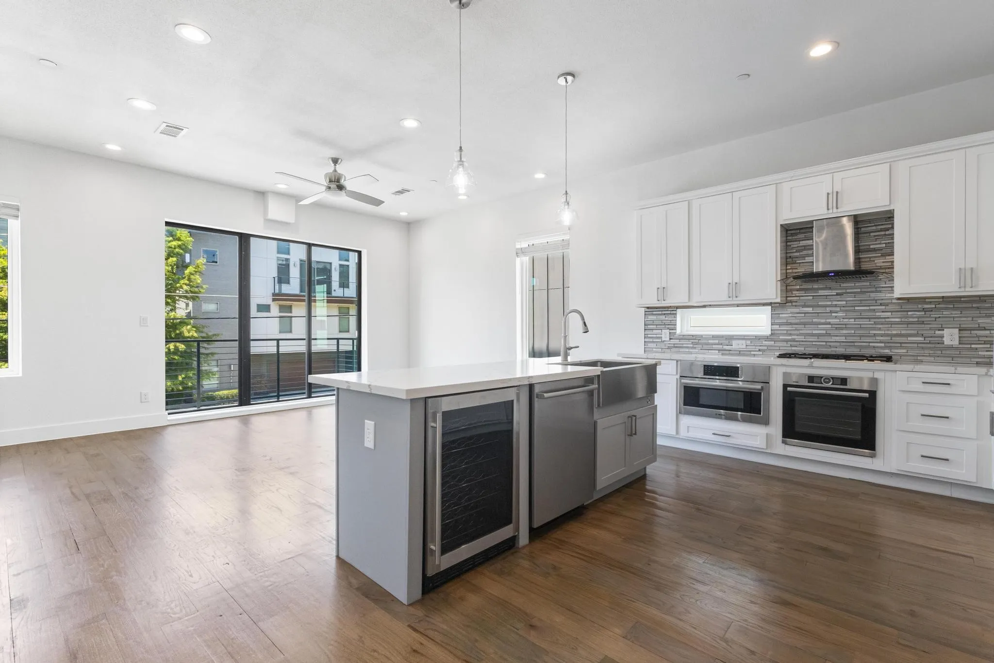 Open-concept living space with wood-finish flooring, a contemporary kitchen, and a large sliding glass door opening to a balcony