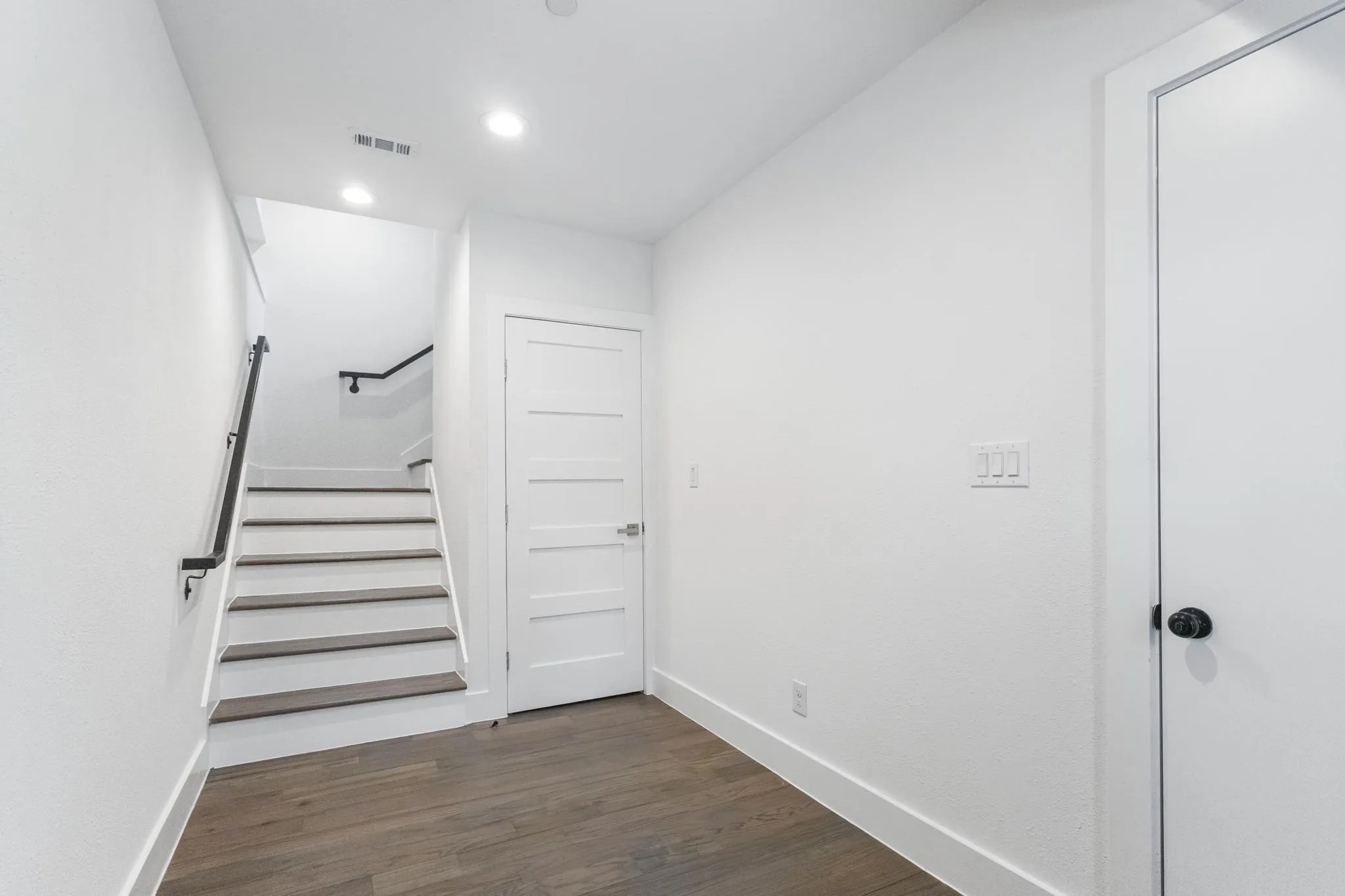 First floor, Hardwood-finish flooring, recessed lighting, modern paneled interior doors, black metal handrail, and white walls