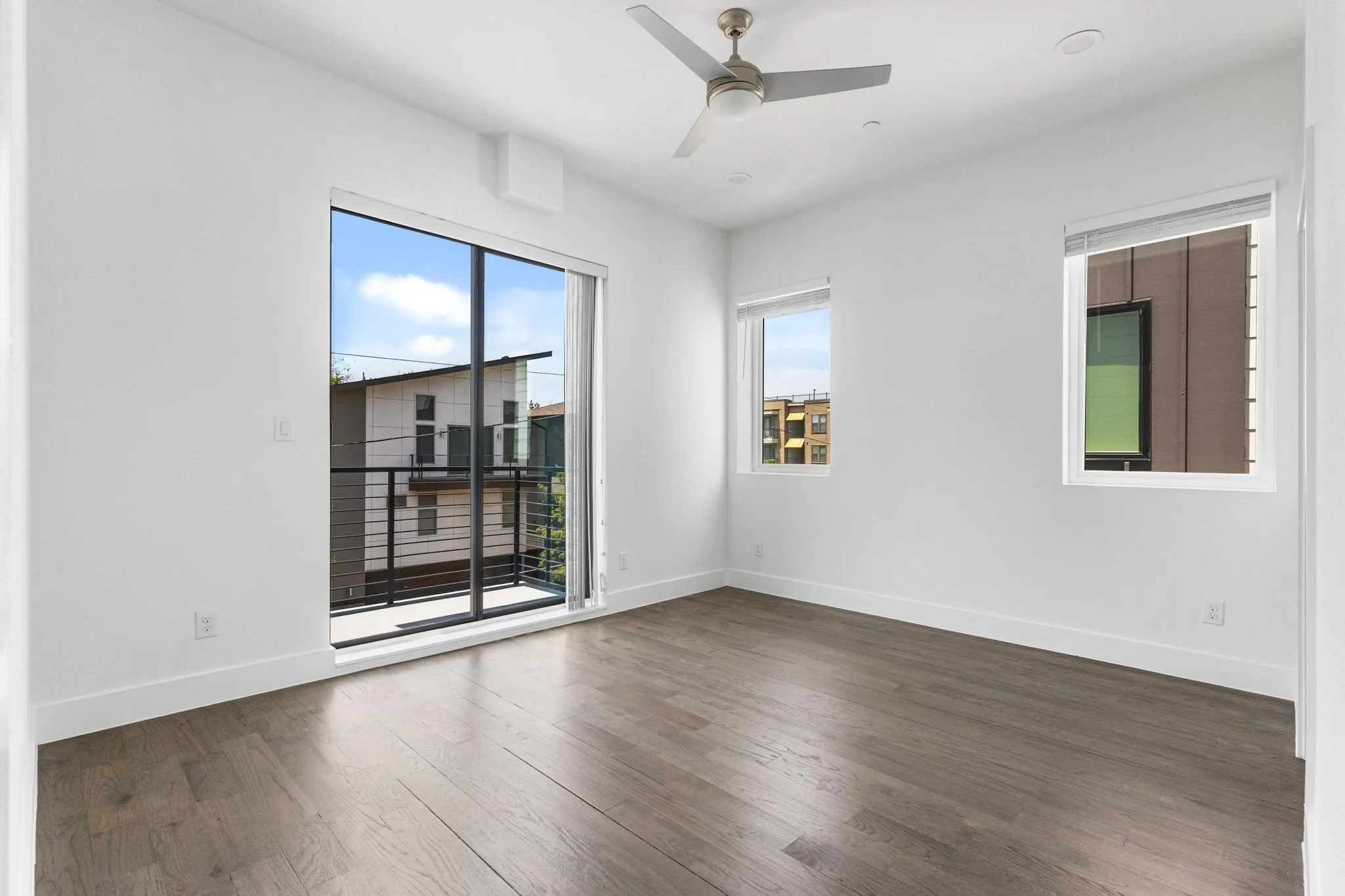 Room featuring wood-finish flooring, a ceiling fan, multiple windows, and a sliding glass door opening to a balcony with metal railing
