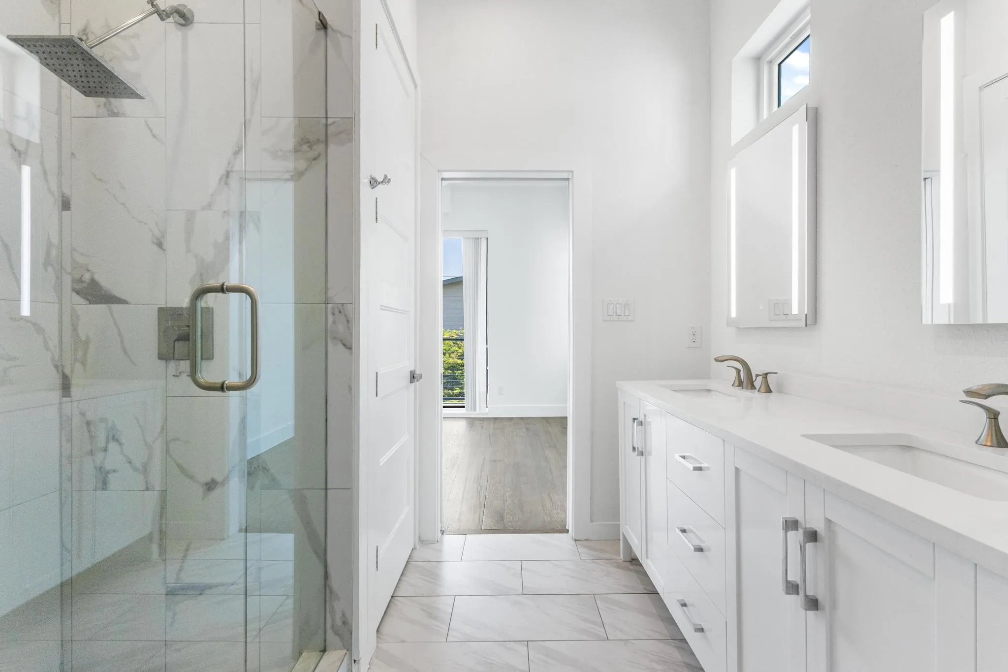 Spacious bathroom featuring a glass-enclosed shower with a rain showerhead, a dual vanity with undermount sinks, and integrated mirror lighting