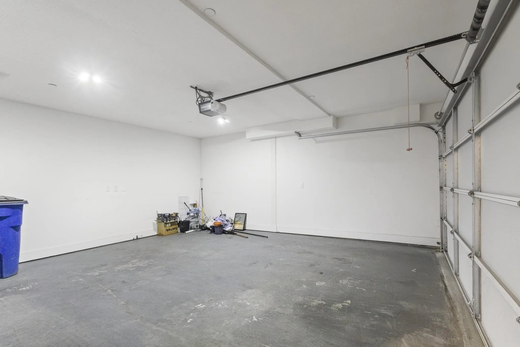 Attached garage with a concrete floor, white walls, and overhead​​‌​​​​‌​​‌‌​‌‌​​​‌‌​‌​‌​‌​​​‌​​ lighting