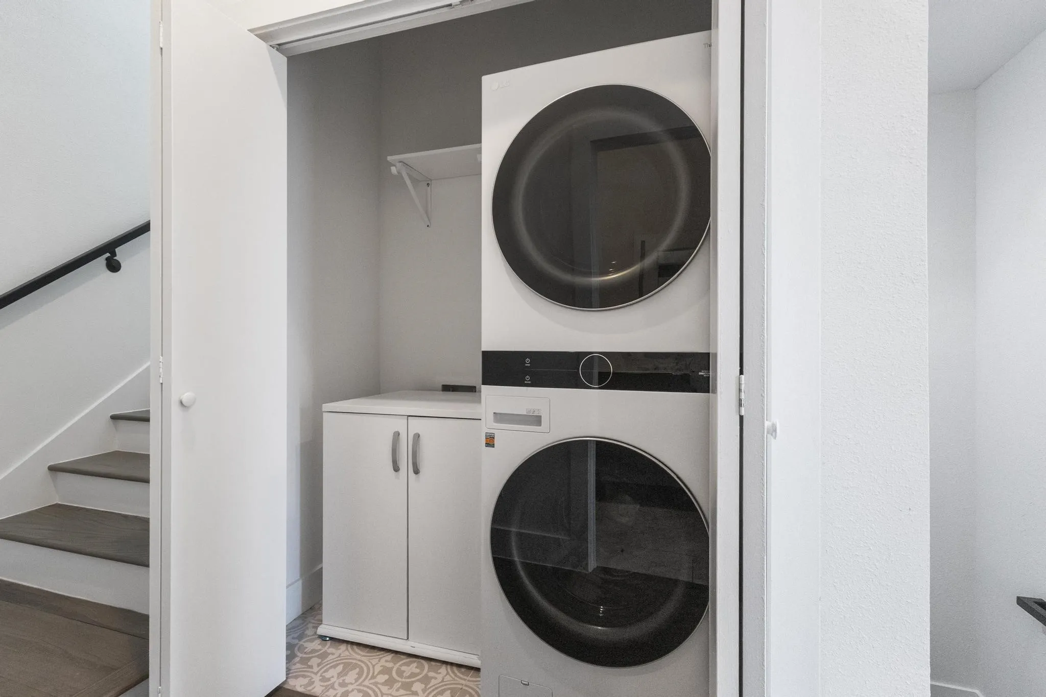 Built-in stackable washer and dryer, adjacent storage cabinet, patterned floor tile, and wall-mounted shelving