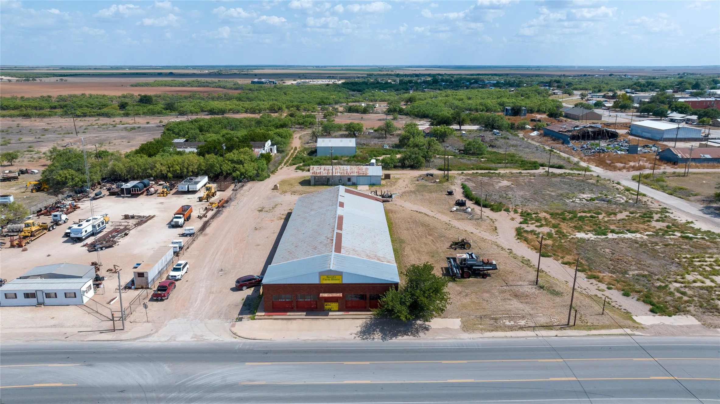 Expansive commercial property featuring a large warehouse structure with a metal roof, an additional detached building, and significant open land