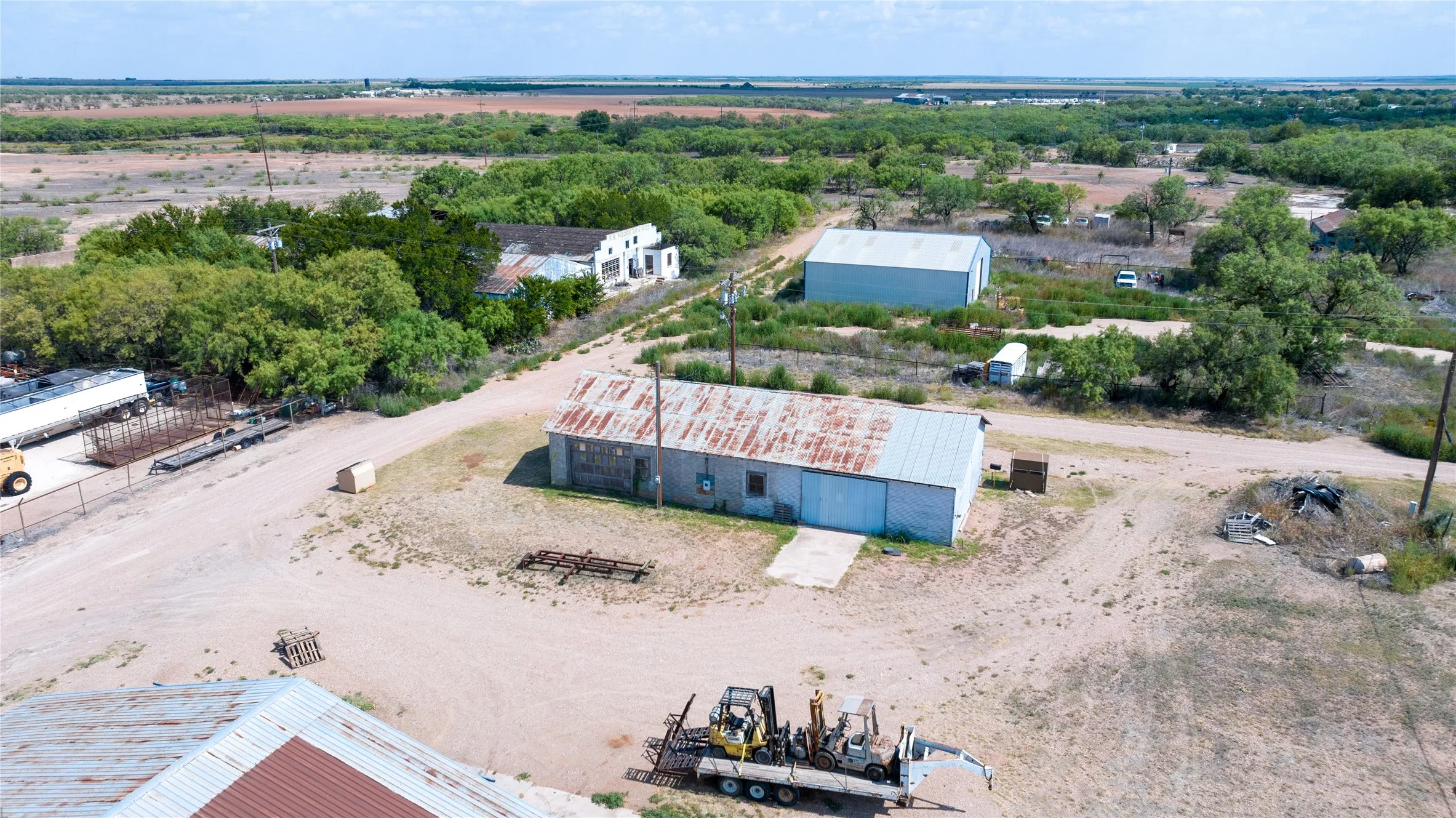 Expansive property featuring multiple outbuildings, mature trees, and a dirt-surfaced drive