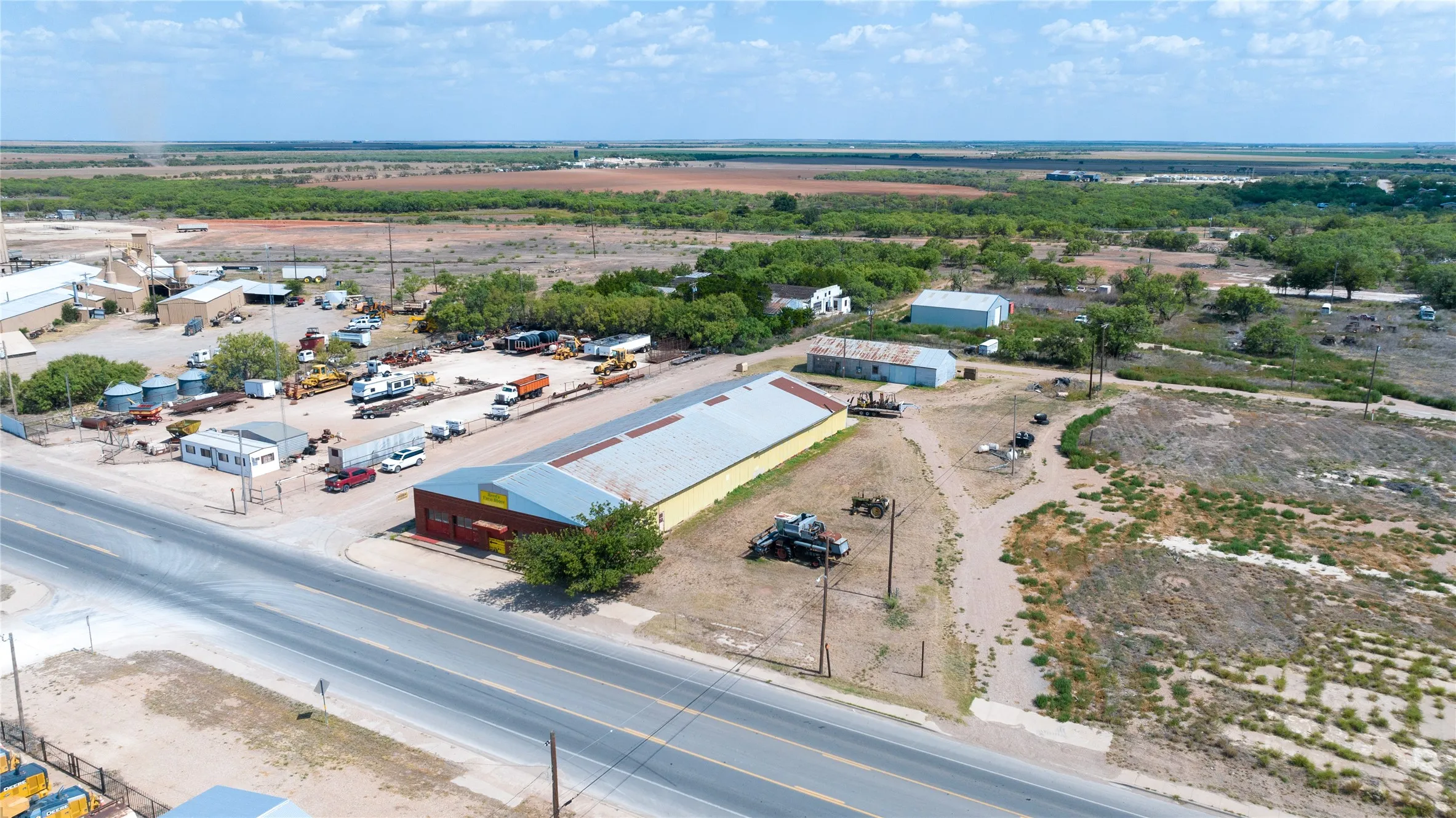Expansive commercial property featuring multiple buildings, paved road frontage, and substantial open land