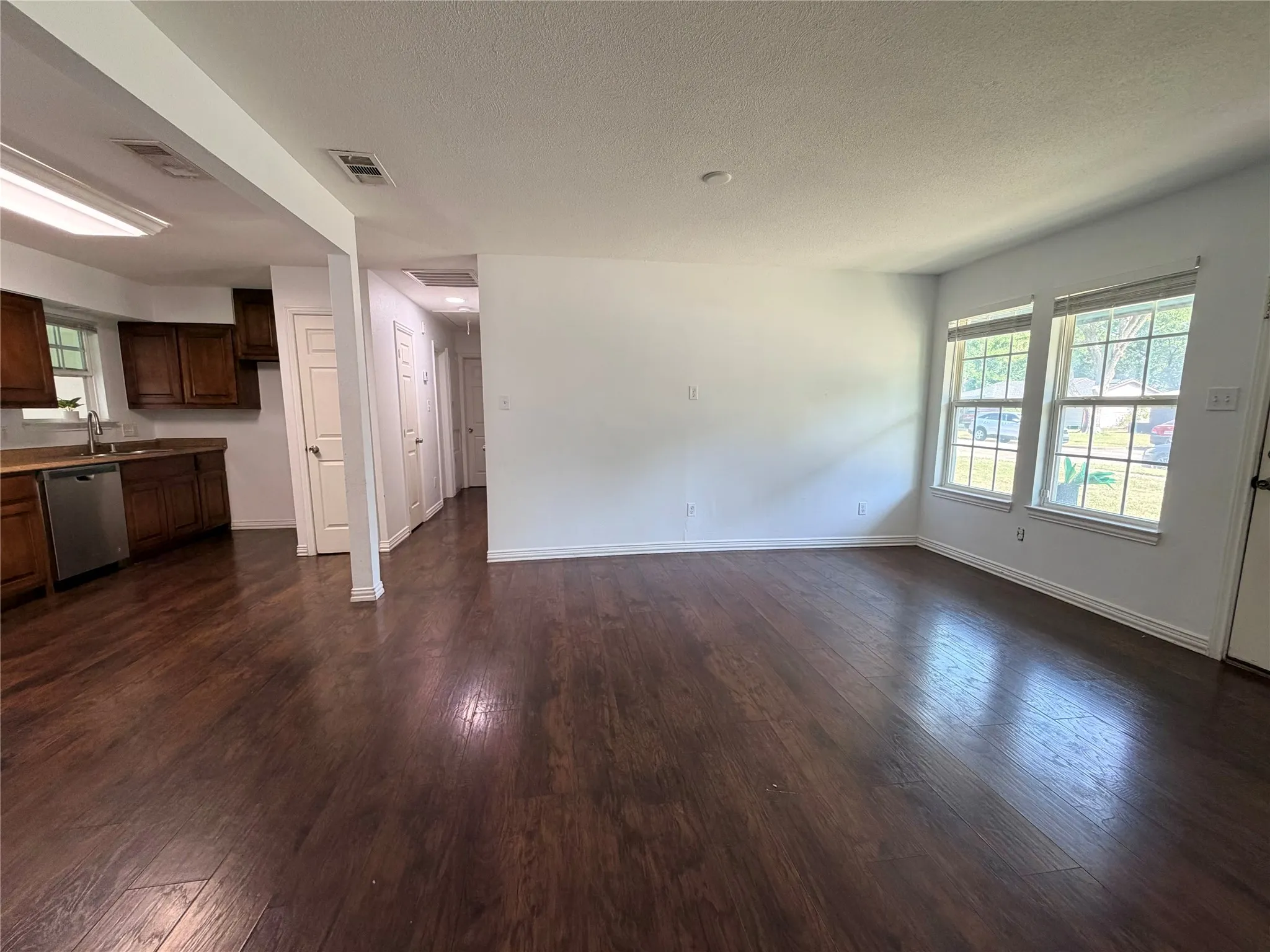Spacious open concept living area featuring dark wood-finish flooring, multiple windows, and a kitchen with wood cabinetry and stainless steel appliances
