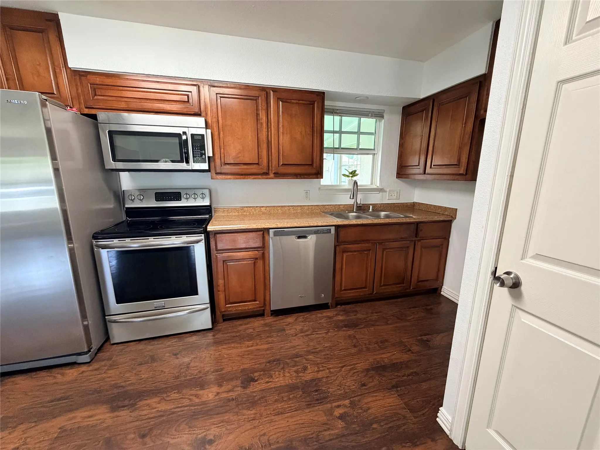 Kitchen featuring wood-finish flooring, wood cabinetry, stainless steel appliances, and a double basin sink