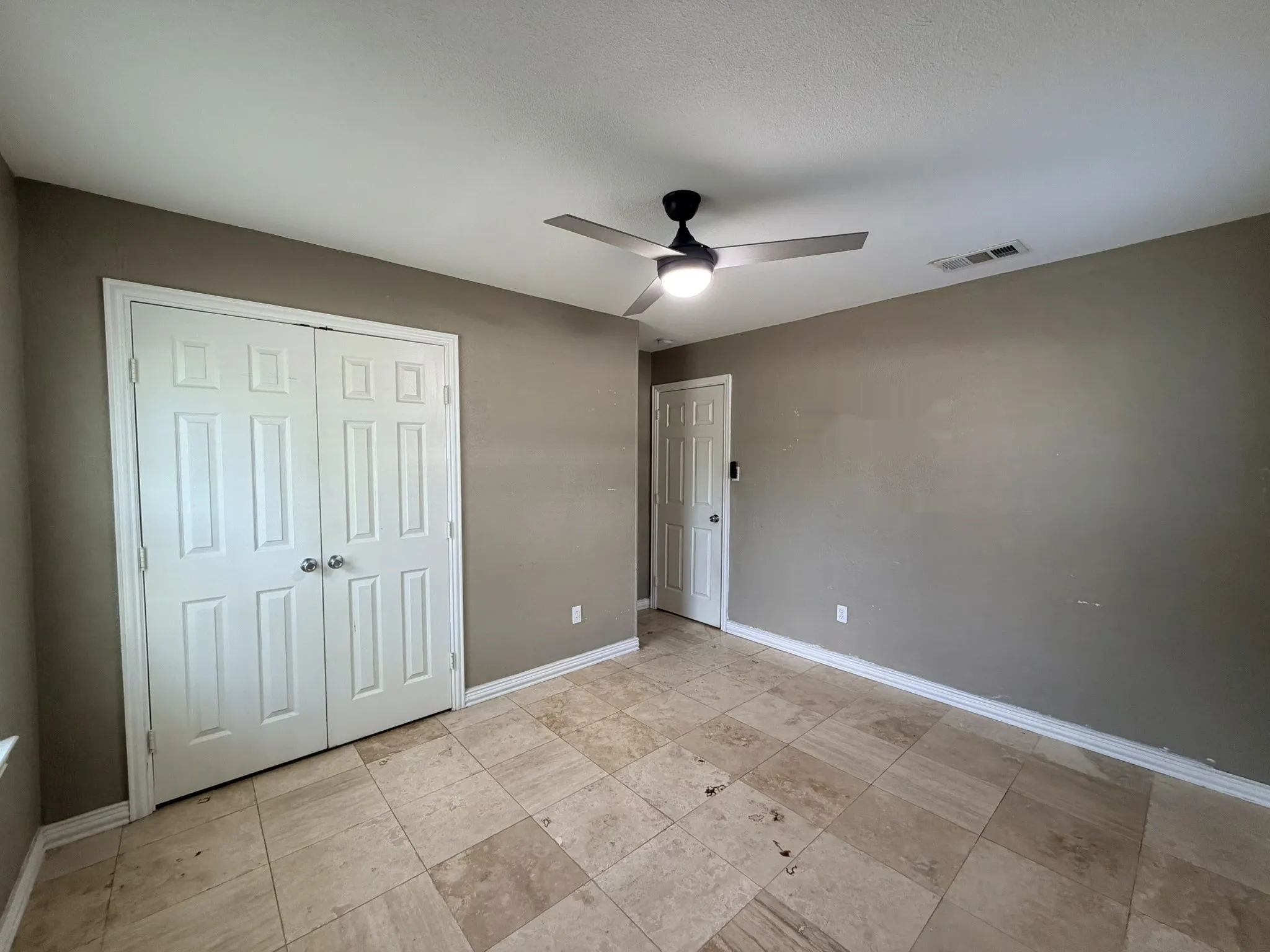 Stone tile flooring, white panel bi-fold closet doors, ceiling fan with integrated lighting, and a white panel door