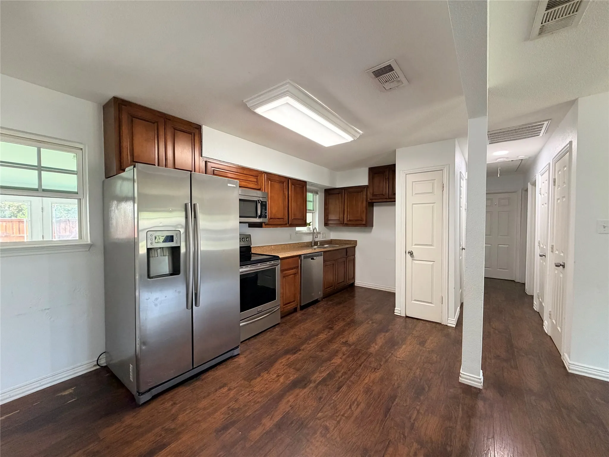Kitchen featuring wood-finish flooring, stainless steel appliances, wood cabinetry, and a window for natural light