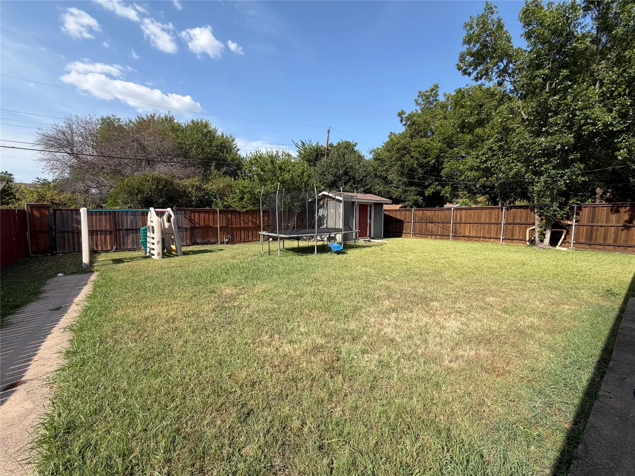 Expansive backyard featuring a privacy fence, mature trees, and a storage shed
