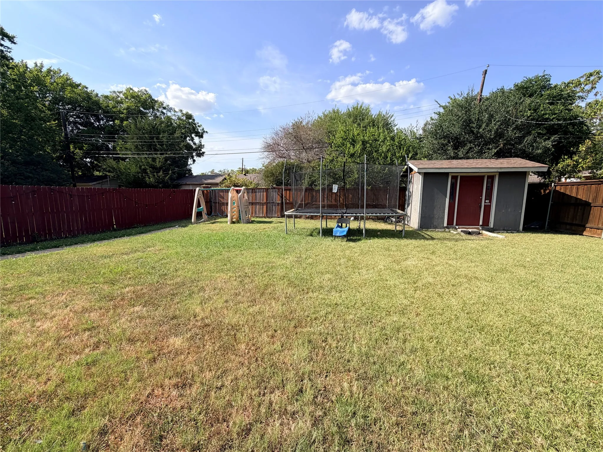 Expansive fenced backyard featuring a storage shed with a red door