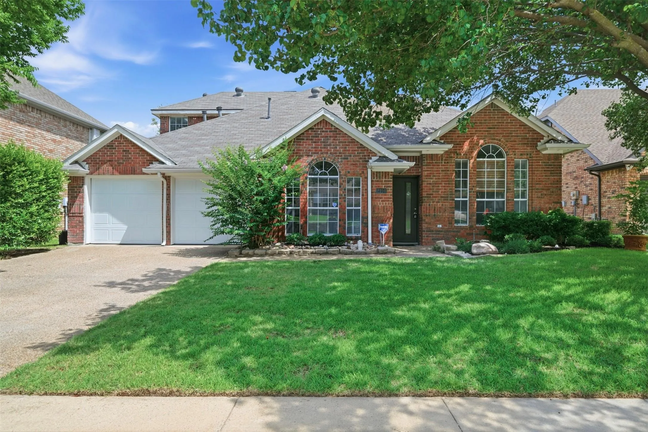 Brick exterior with decorative arched windows, an attached two-car garage, mature landscaping, and a well-maintained lawn