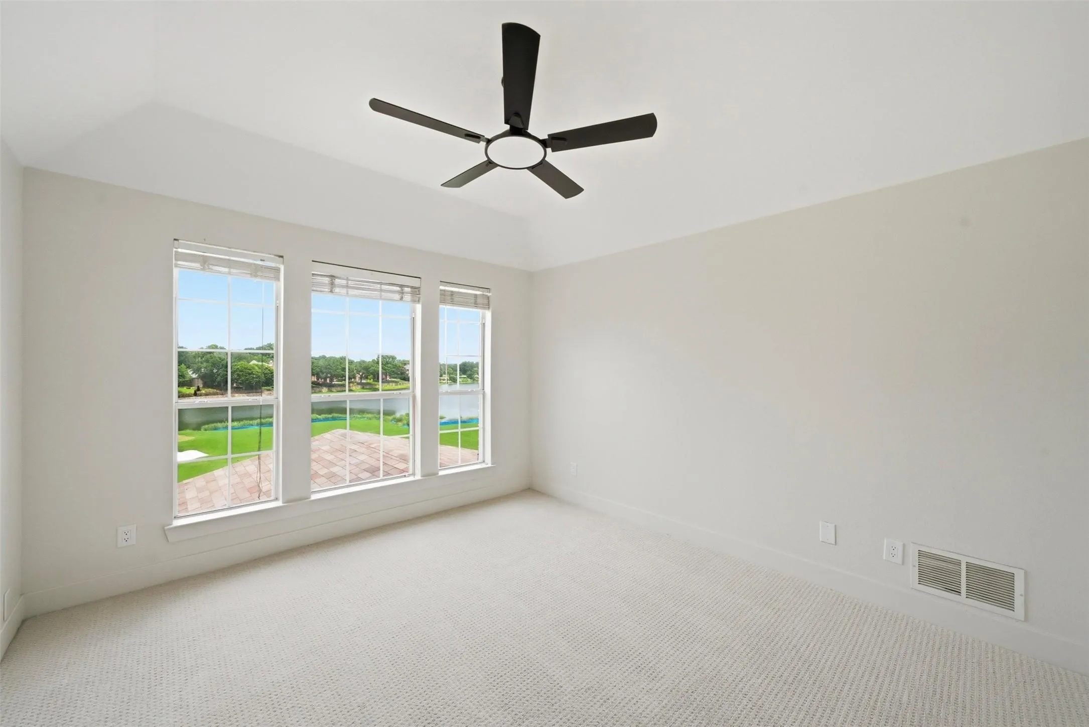 Vaulted ceiling with a black ceiling fan, white walls, and light-colored carpeting