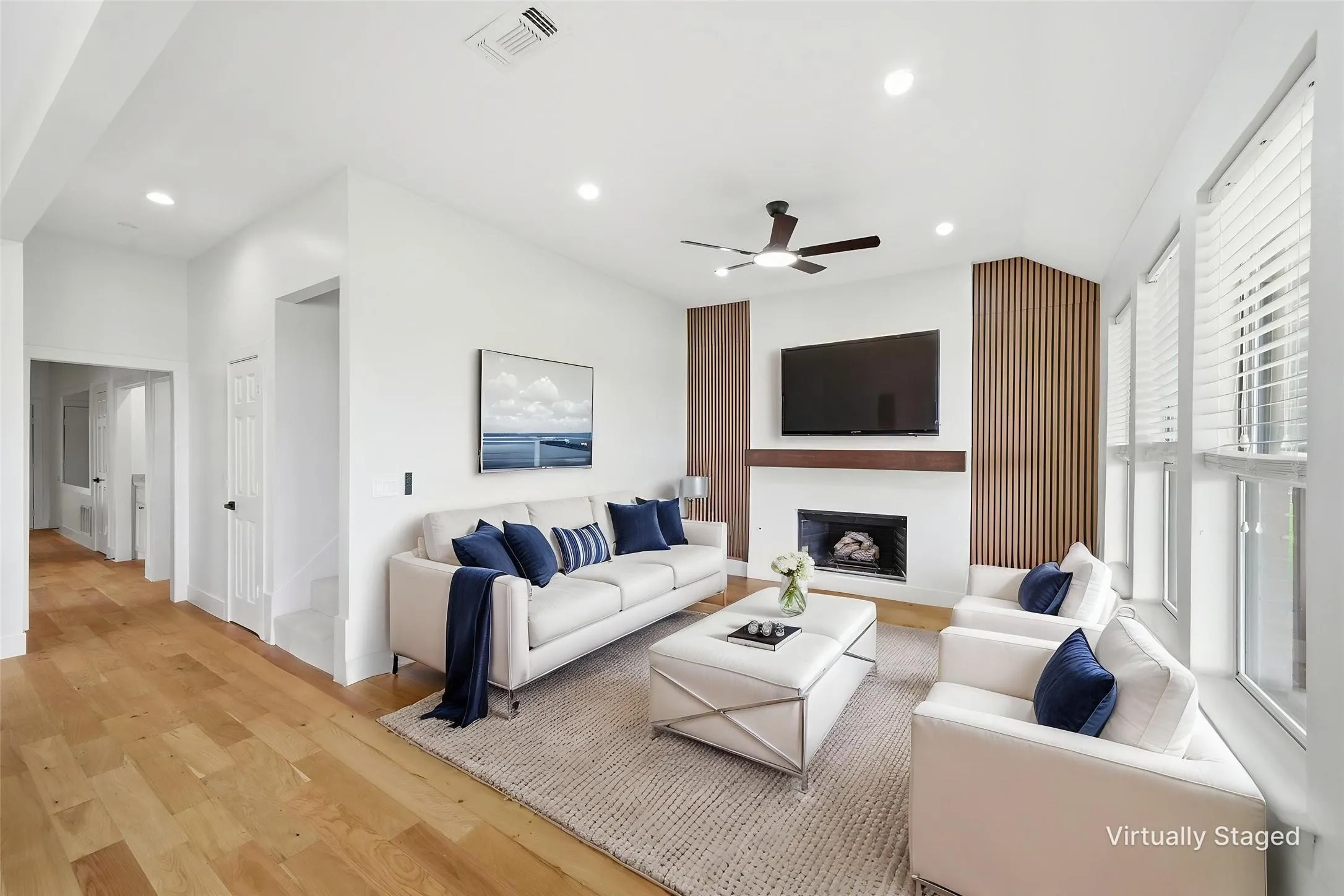 Living area featuring wood-finish flooring, a contemporary fireplace with a white mantel, and a ceiling fan with integrated lighting