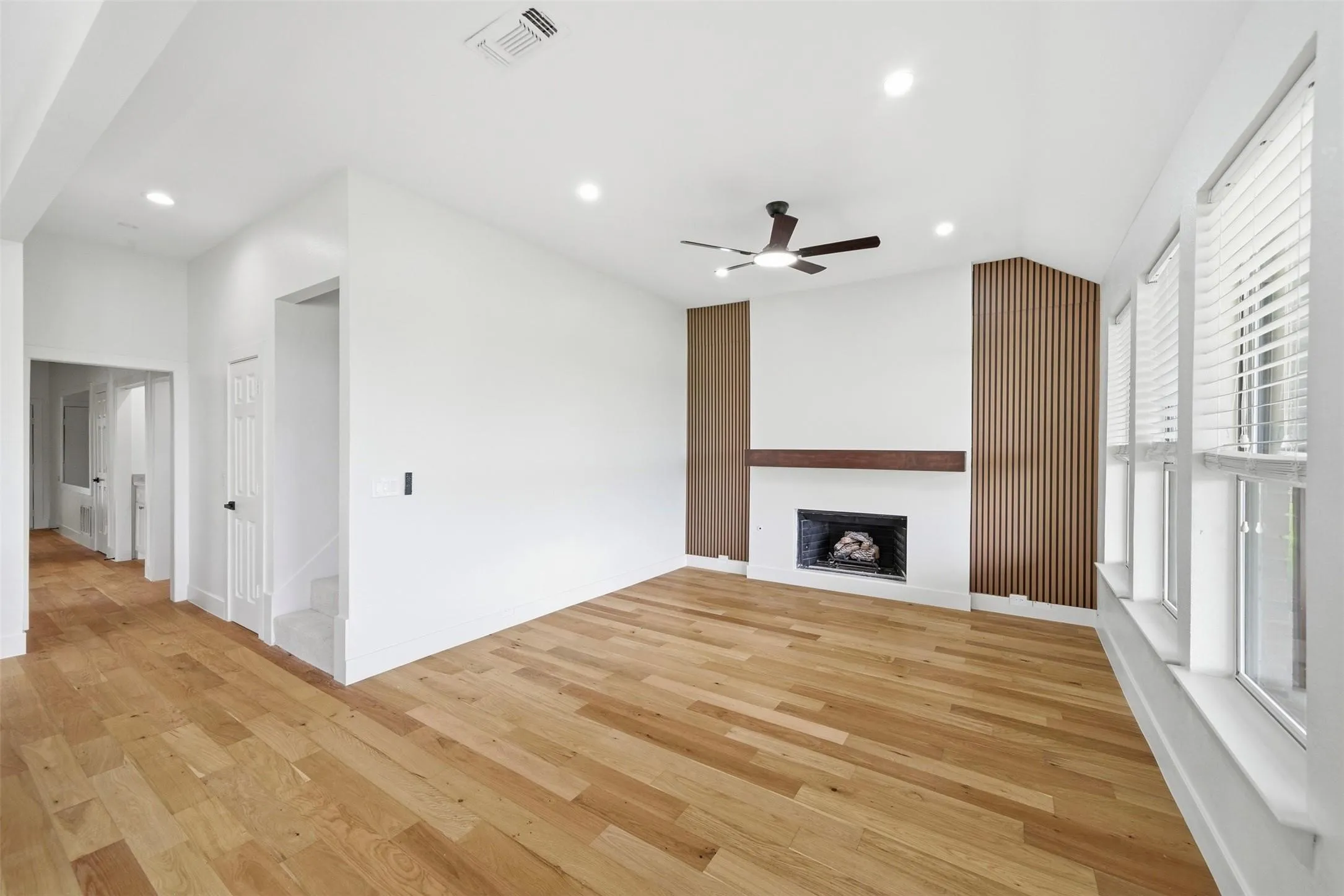 Spacious living area featuring wood-finish flooring, a fireplace with a wood mantle, and multiple windows with blinds