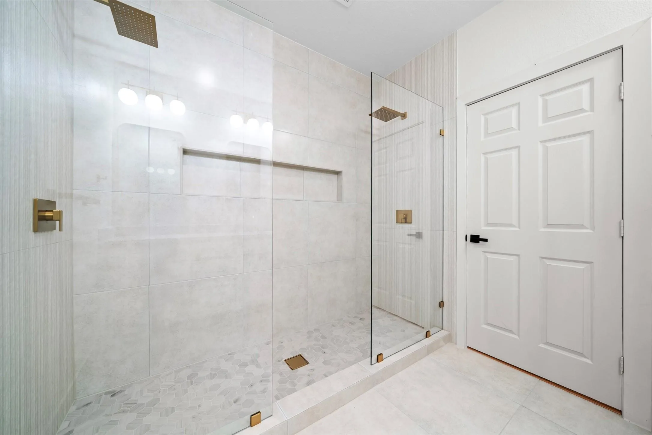 Glass-enclosed shower featuring a built-in niche, gold-finish fixtures, and a pebble tile shower floor
