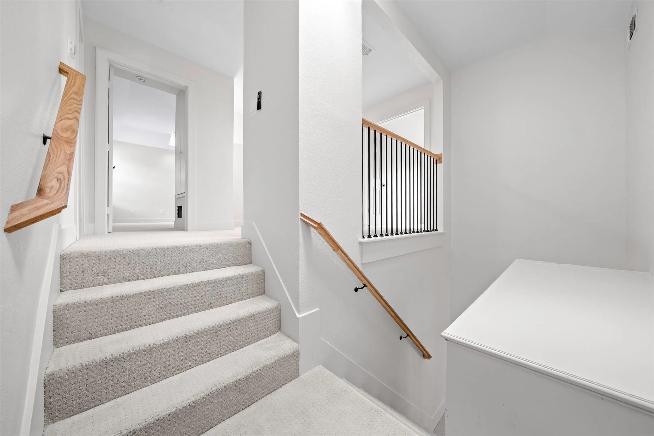 Carpeted staircase with wood handrails, black metal balusters, and white wall finishes