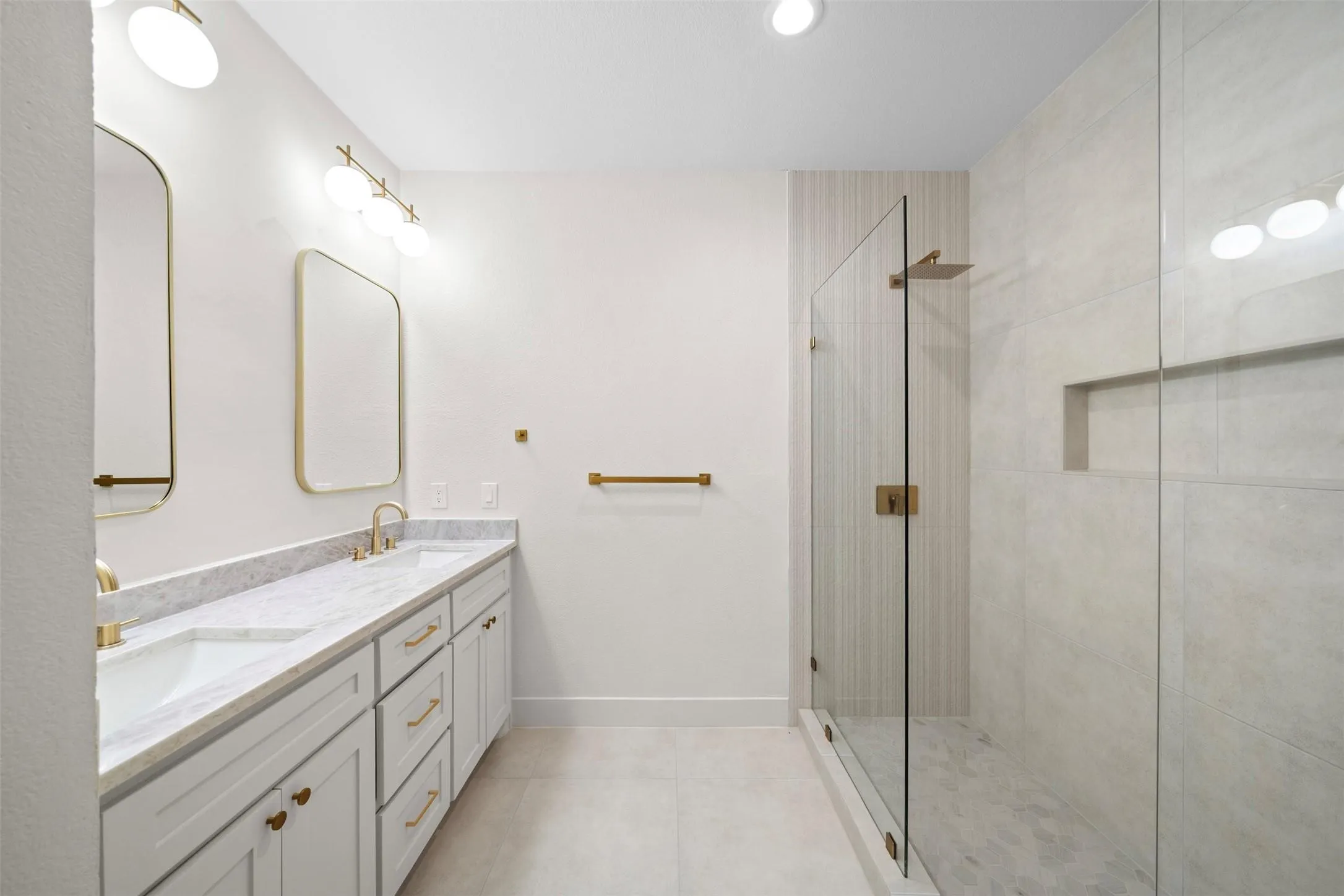 Dual vanity with integrated sinks and a stone countertop, framed mirrors, glass-enclosed shower, shower niche, and gold-finish fixtures