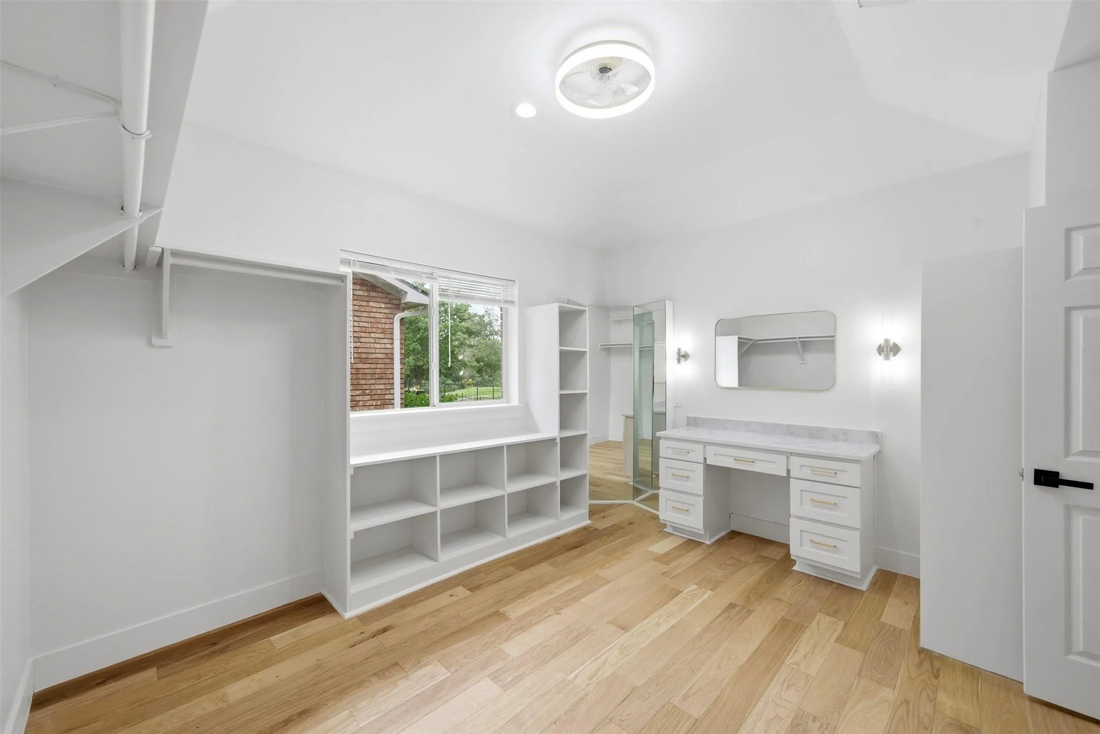 Natural wood-finish flooring, built-in shelving, white cabinetry with a stone countertop, wall-mounted sconces, and a flush-mount ceiling light