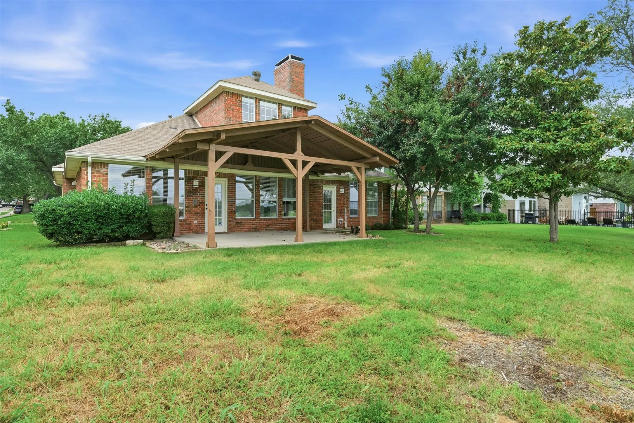 Brick exterior, covered patio, multiple windows, established trees, and green lawn