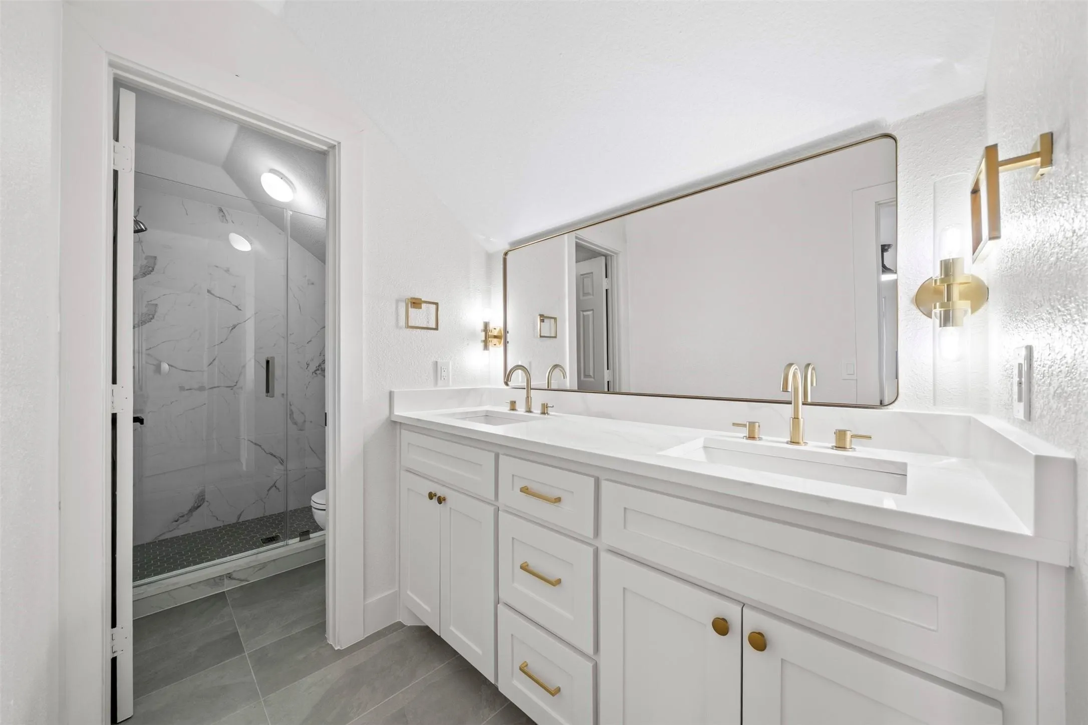 Dual vanity with integrated sinks, white cabinetry, gold-finish hardware, and a large rectangular mirror