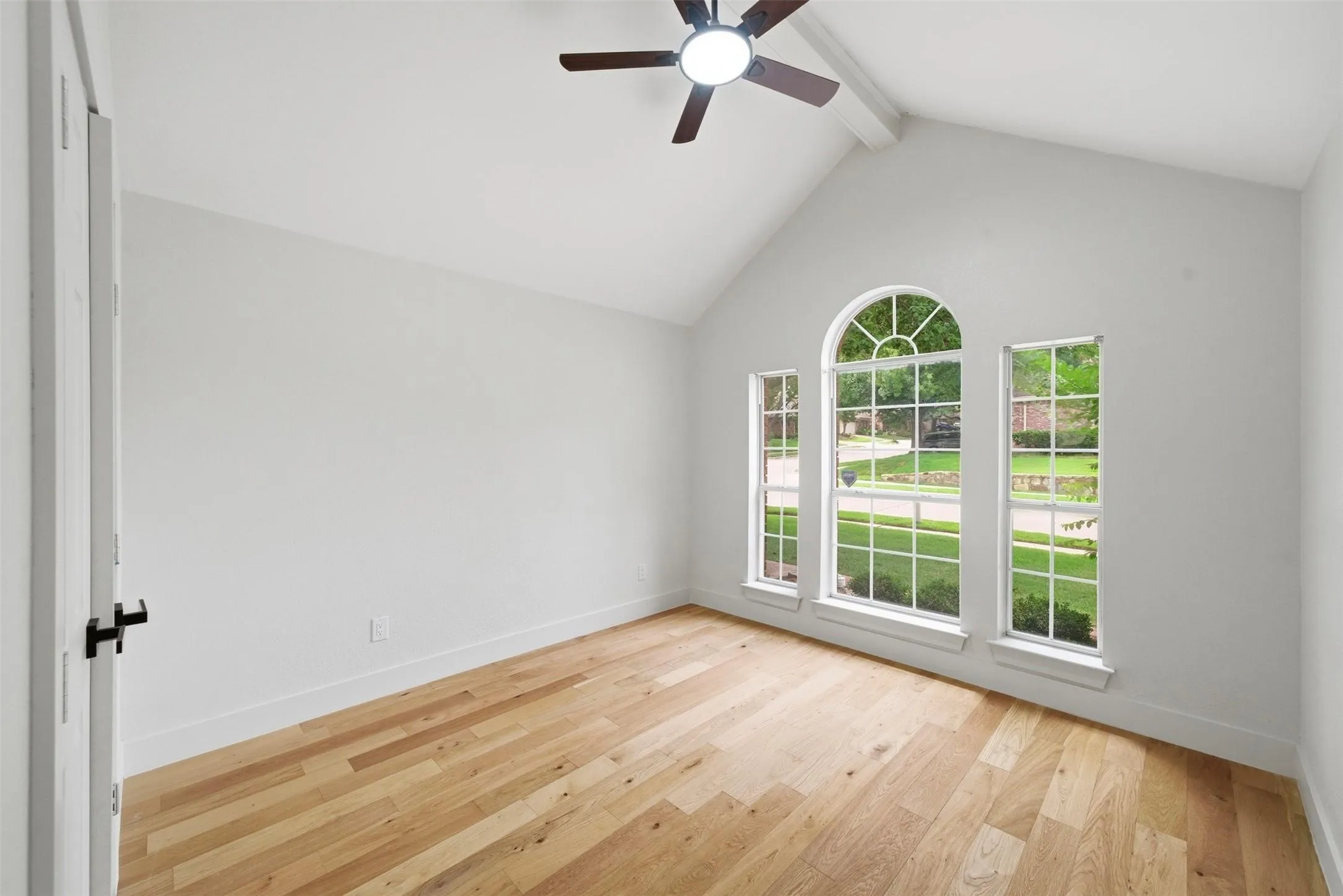 Vauted ceiling with exposed beam, wood-finish flooring, and arched window