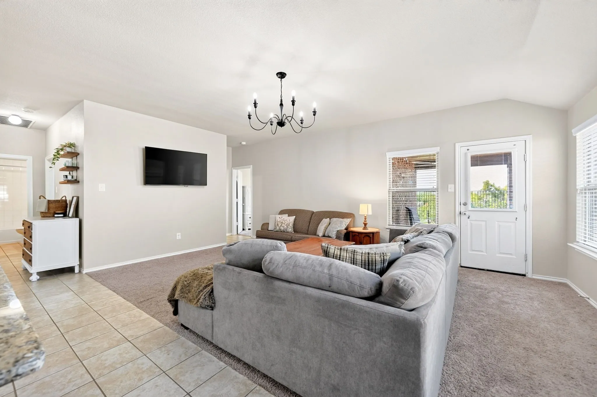 Spacious open-concept living area with neutral wall finishes, tile and carpeted flooring throughout, and abundant natural light from multiple glass doors and windows