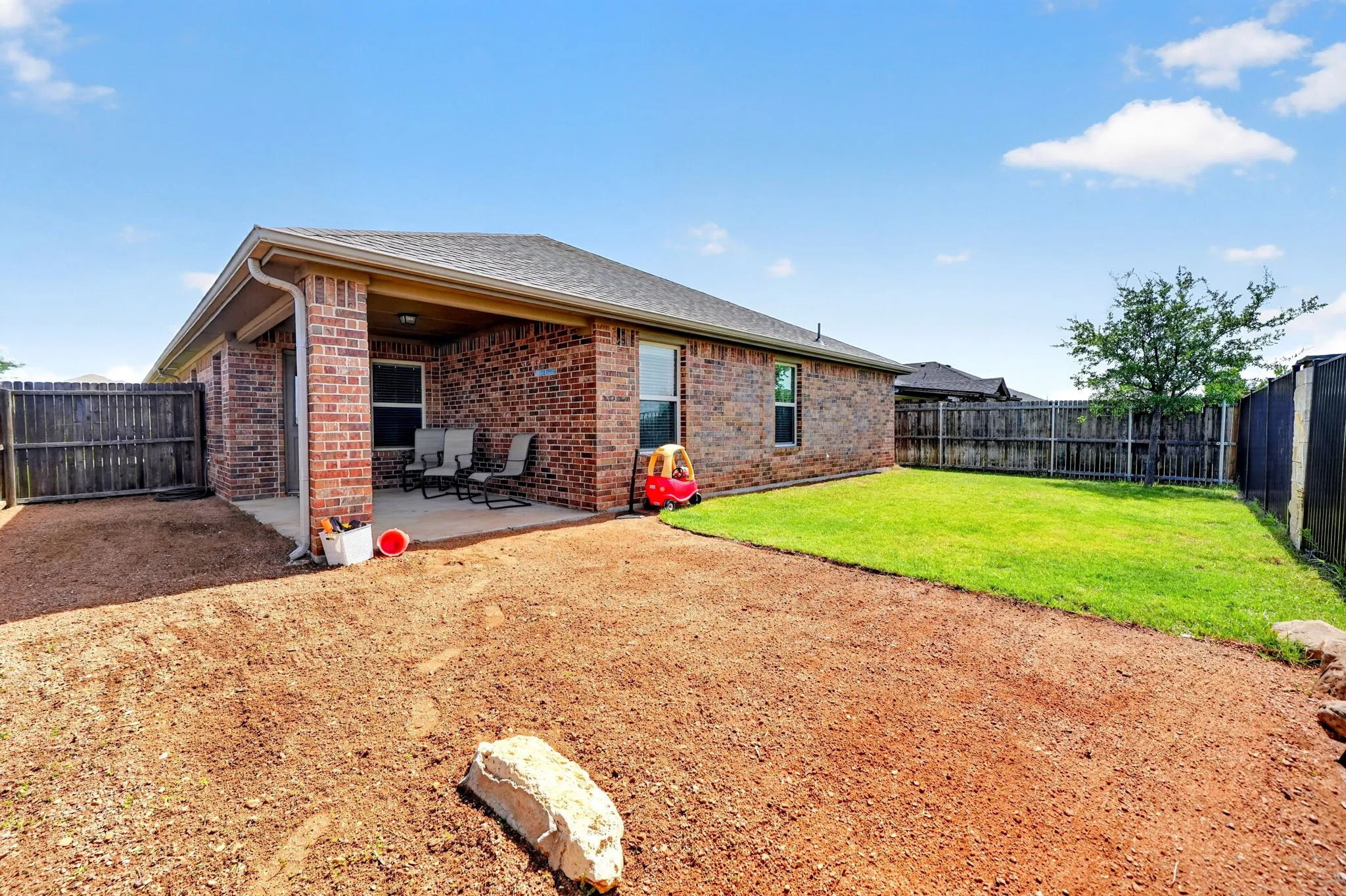 Brick exterior with covered patio, concrete flooring, and an expansive lawn