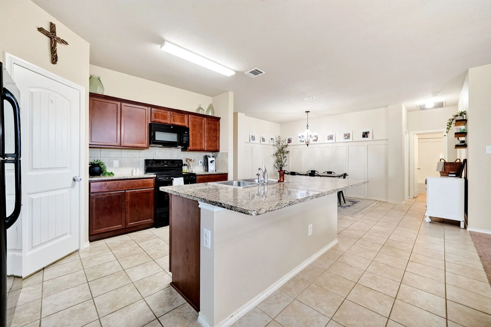 Kitchen featuring a granite-topped island with an undermount sink, wood cabinetry, tile flooring, and a subway tile backsplash