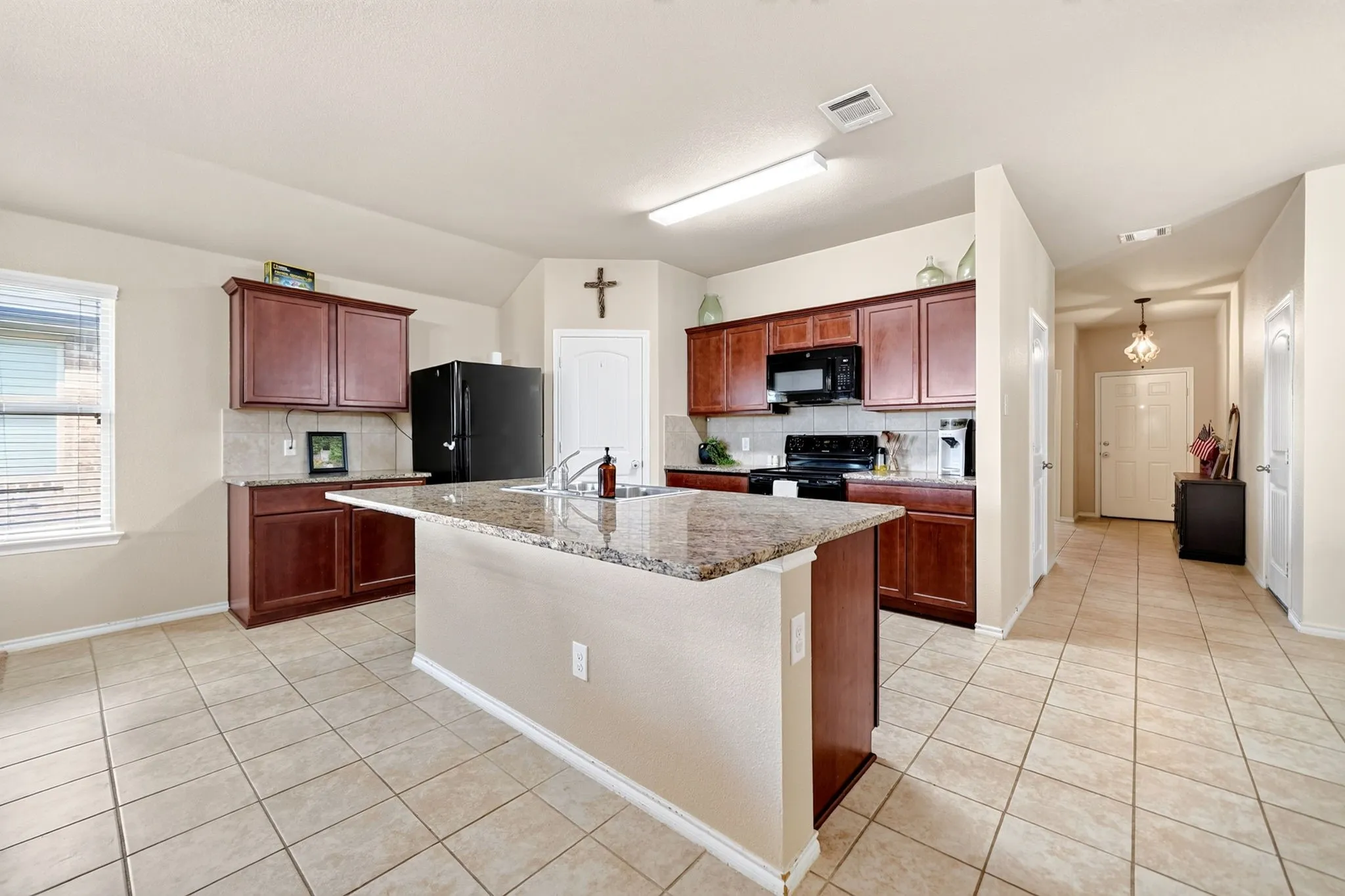 Kitchen featuring an island with a built-in sink, dark wood cabinetry, and tiled flooring