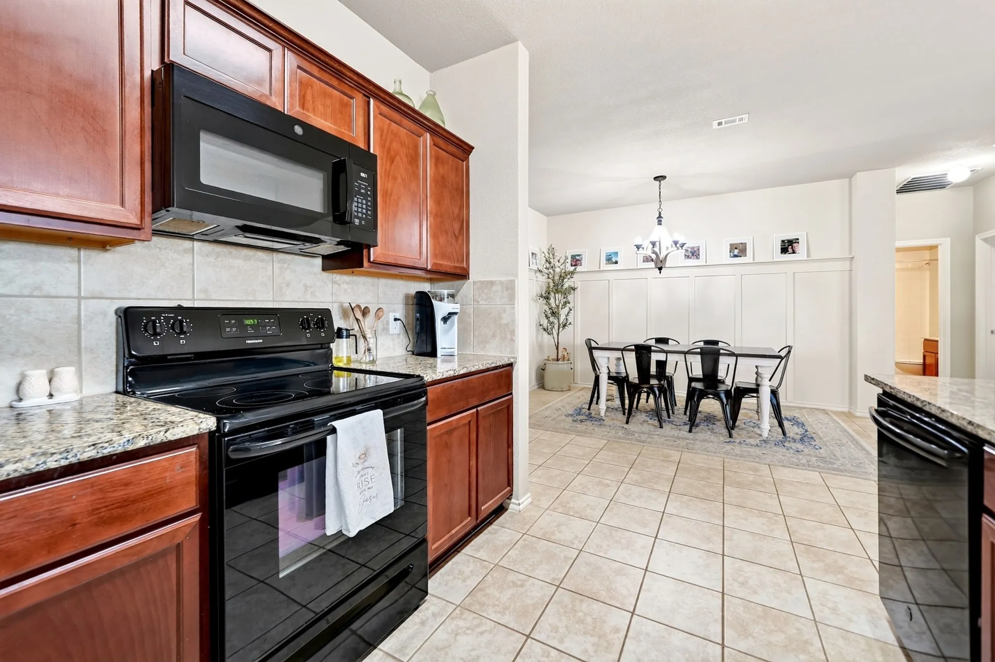 Tile flooring throughout, wood-finish cabinetry, black appliances, stone countertops, and a dining area with wainscoting