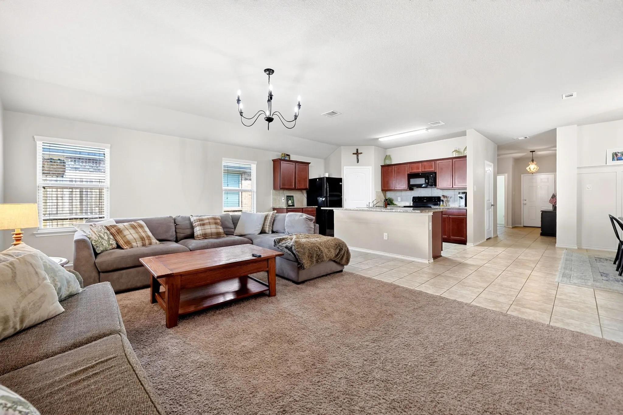 Open-concept living area with carpet flooring and an adjacent kitchen featuring wood cabinetry, stone-finish countertops, and black appliances
