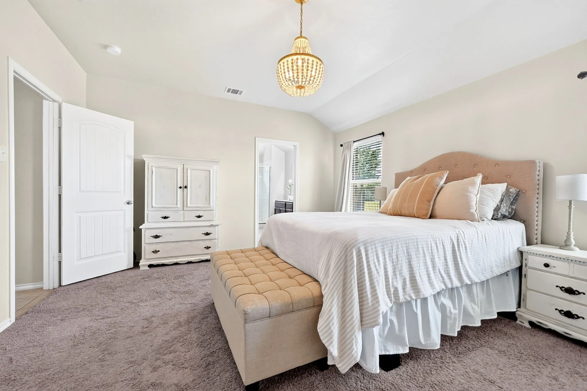 Vaulted ceiling with an ornate chandelier, neutral tone walls, white paneled door, and a window with blinds