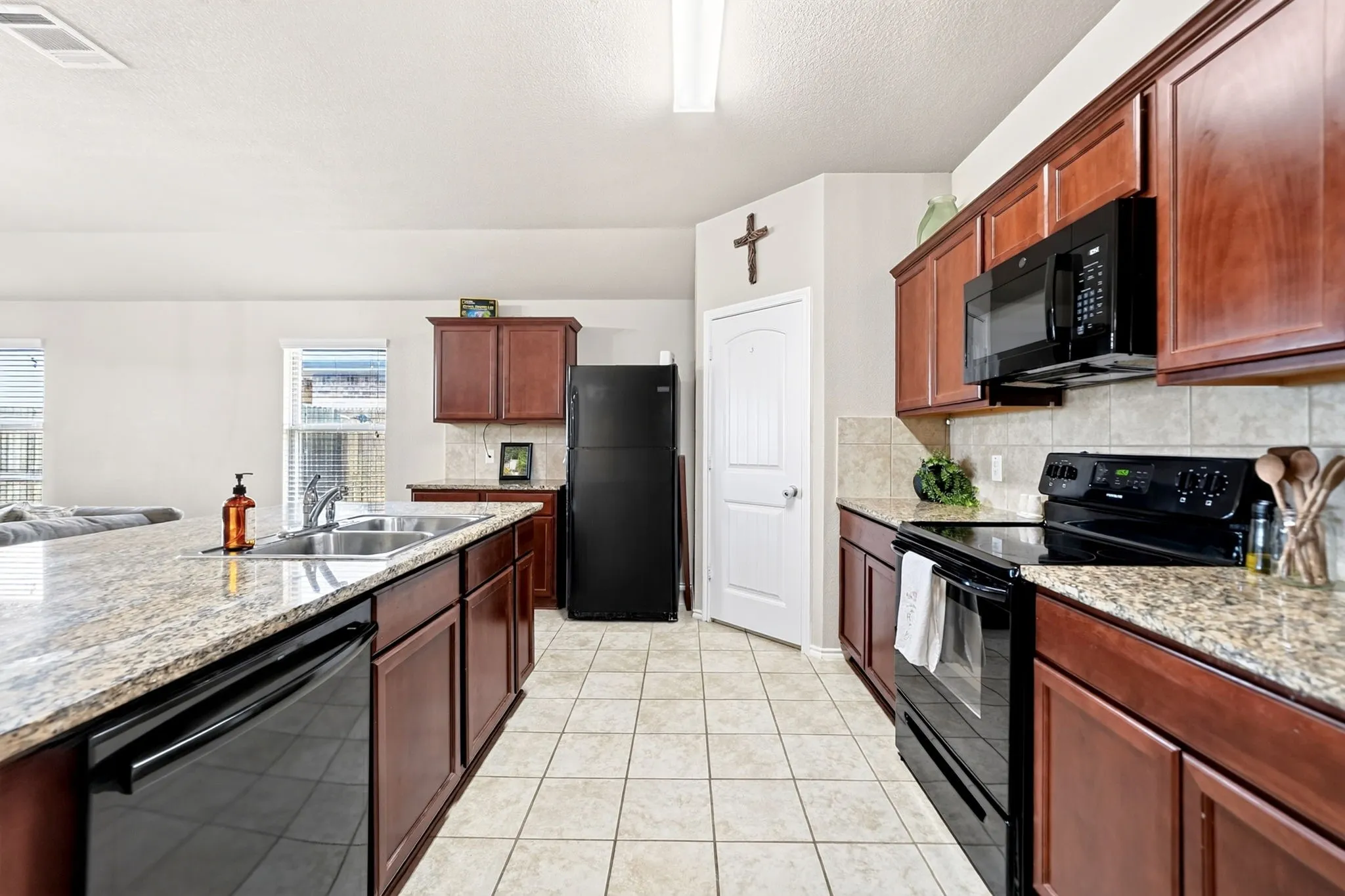 Kitchen featuring wood cabinetry, black appliances, light-toned tile flooring, and light-colored countertops